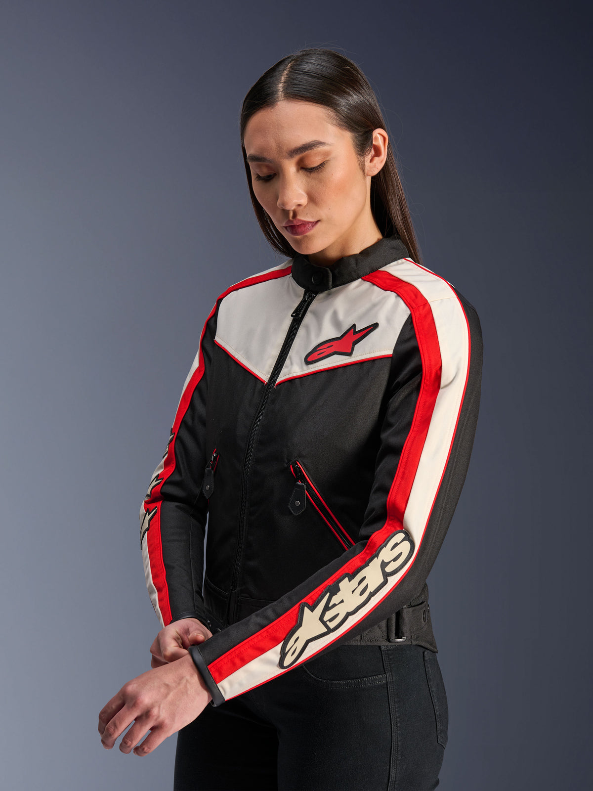 Alpinestars Stella T-Dyno WR Jacke, Motorrad-Textiljacke für Damen, Schwarz, Ecru und Bright Red, vintage-inspiriertes Design mit rotem Alpinestars-Logo auf der Brust und Branding auf dem Ärmel, getragen von einem Model in einer Studioumgebung.