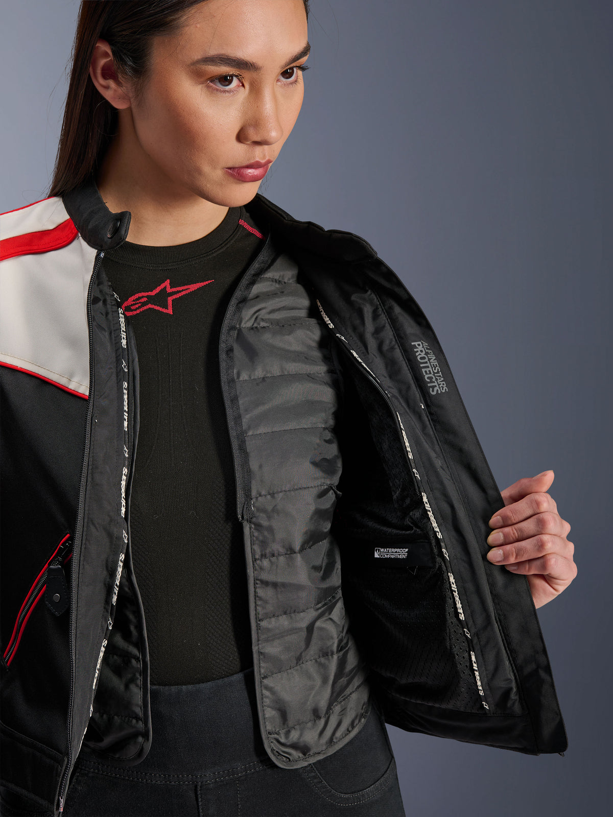 Alpinestars Stella T-Dyno WR Jacke, Damen-Motorradjacke, Schwarz, Ecru und Hellrot, Nahaufnahme der Innenseite mit abnehmbarer gesteppter Thermoweste, wasserdichtem Innenfach und „ALPINESTARS PROTECTS“-Branding.