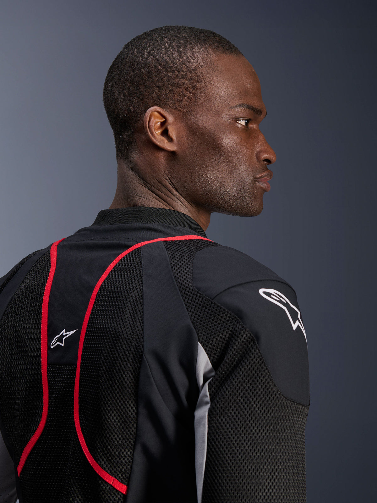 Alpinestars Troop-Air Pro Jacke, technische gepanzerte Air-Jacke, Schwarz, Ash Gray und Bright Red, Nahaufnahme von Profil und Rückenansicht mit Mesh-Textileinsätzen, roten Paspel-Akzenten und weißen Astars-Logos auf der Schulter und dem oberen Rücken