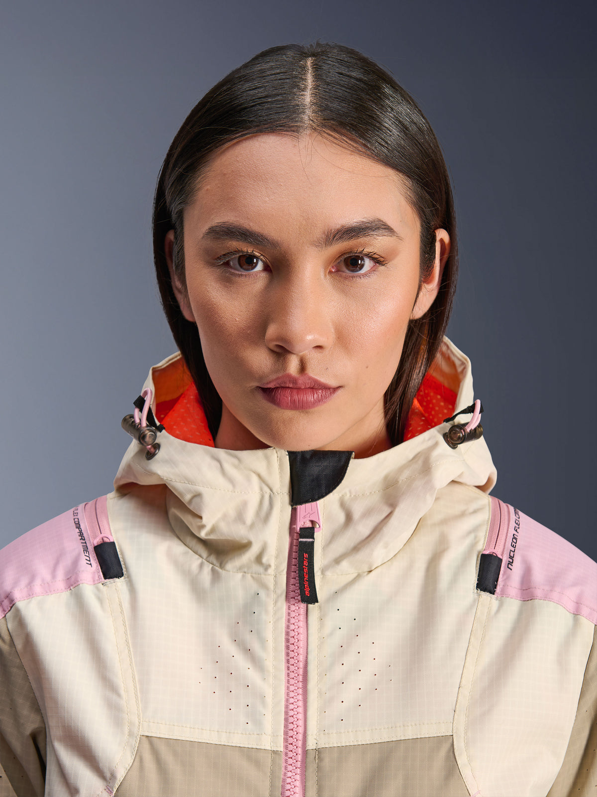 Nahaufnahme eines weiblichen Models in der Alpinestars Molly Air Jacke in Sand Pink Almond, mit hohem Kragen und Kapuze mit leuchtend orangefarbenem Innenfutter, rosafarbenem Frontreißverschluss, Ripstop-Gewebe mit laserperforiertem Brustbereich zur Belüftung, urbane Motorrad-Schutzausrüstung