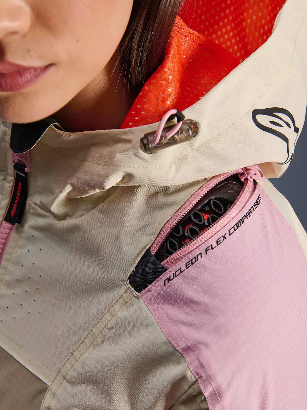 Alpinestars Molly Air Jacke in Sand Pink Almond, Nahaufnahme, Schulterfach mit Reißverschluss für Nucleon Flex Protektoren, leuchtend oranges Mesh-Kapuzenfutter, strapazierfähiges Ripstop-Gewebe.