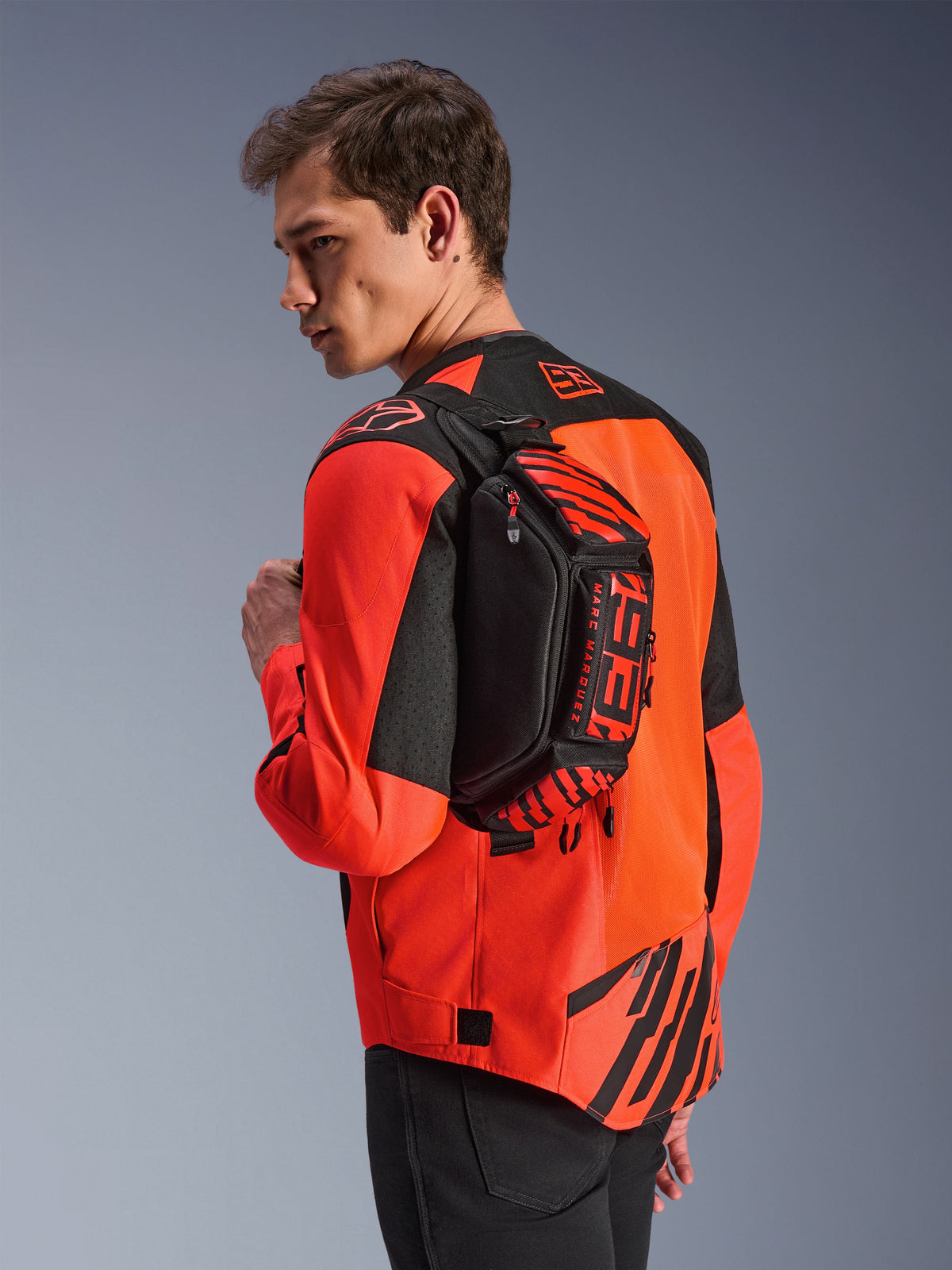 Alpinestars MM93 Hüfttasche, Schwarz mit Red Fluo und Bright Red, von einem Model über dem Rücken über einer rot-schwarzen Motorradjacke getragen, mit markantem MM93-Branding und Marc-Marquez-Grafiken