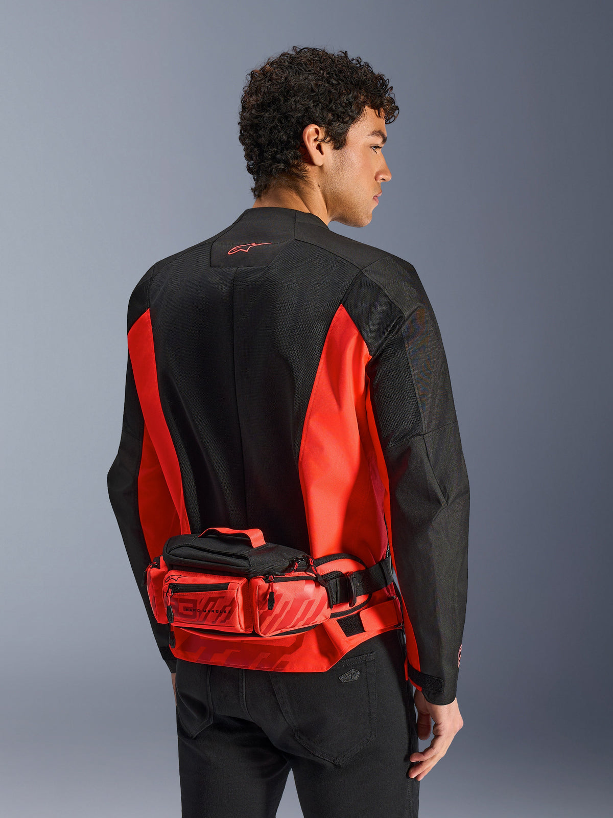 Alpinestars MM93 Waist Bag, Motorcycle Waist Pack, Bright Red and Black, worn over a matching black and red riding jacket, featuring zippered compartments and Marc Marquez MM93 branding, durable textile construction for motorcycling