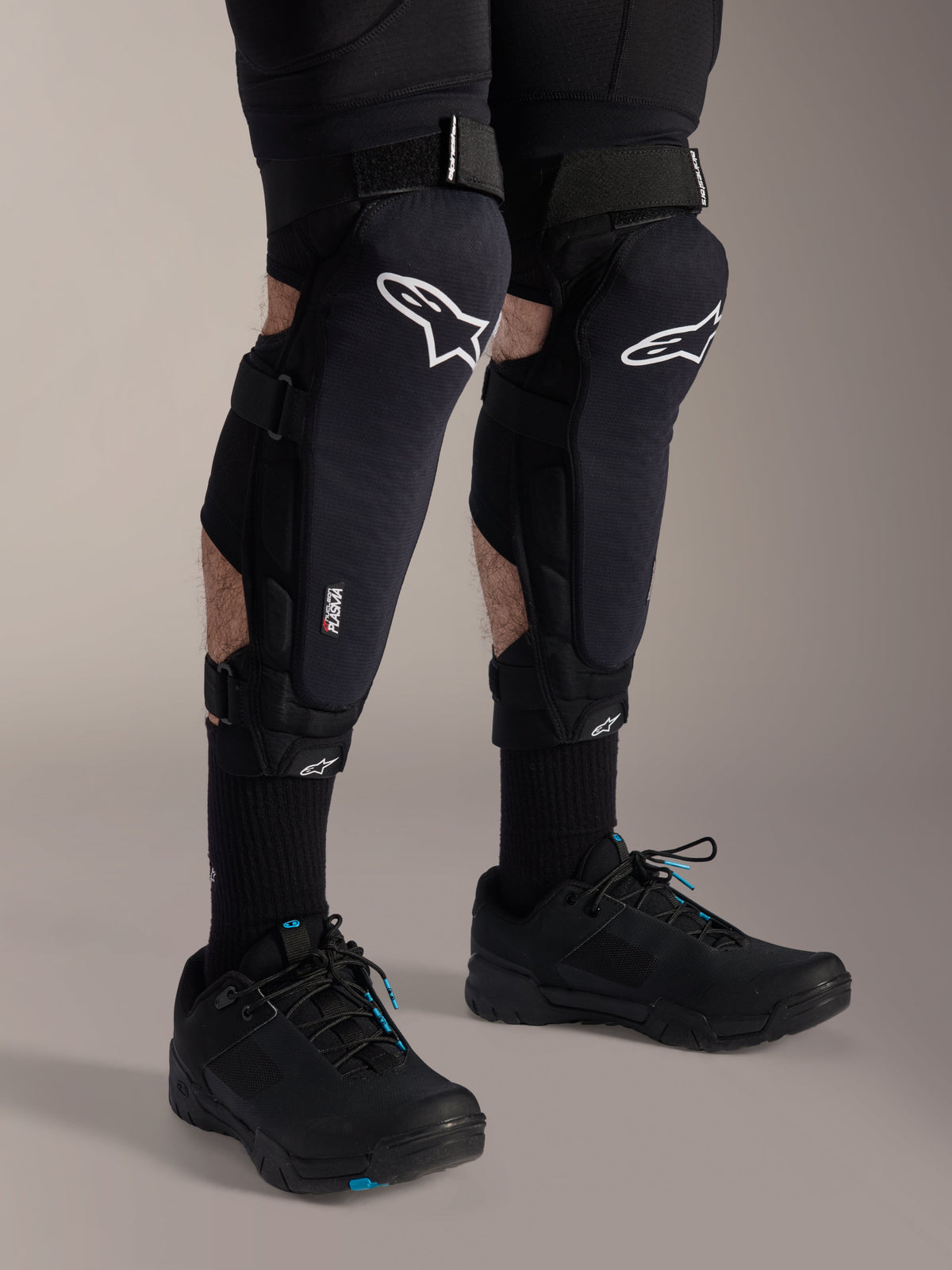 Alpinestars A-Impact Plasma Pro Knieschützer, Schwarz und Weiß, mit Nucleon PLASMA Technologie-Branding, getragen mit schwarzen Socken und schwarzen Mountainbike-Schuhen, sichere Klettverschlussriemen, ergonomische Schutzausrüstung für den Offroad-Radsport