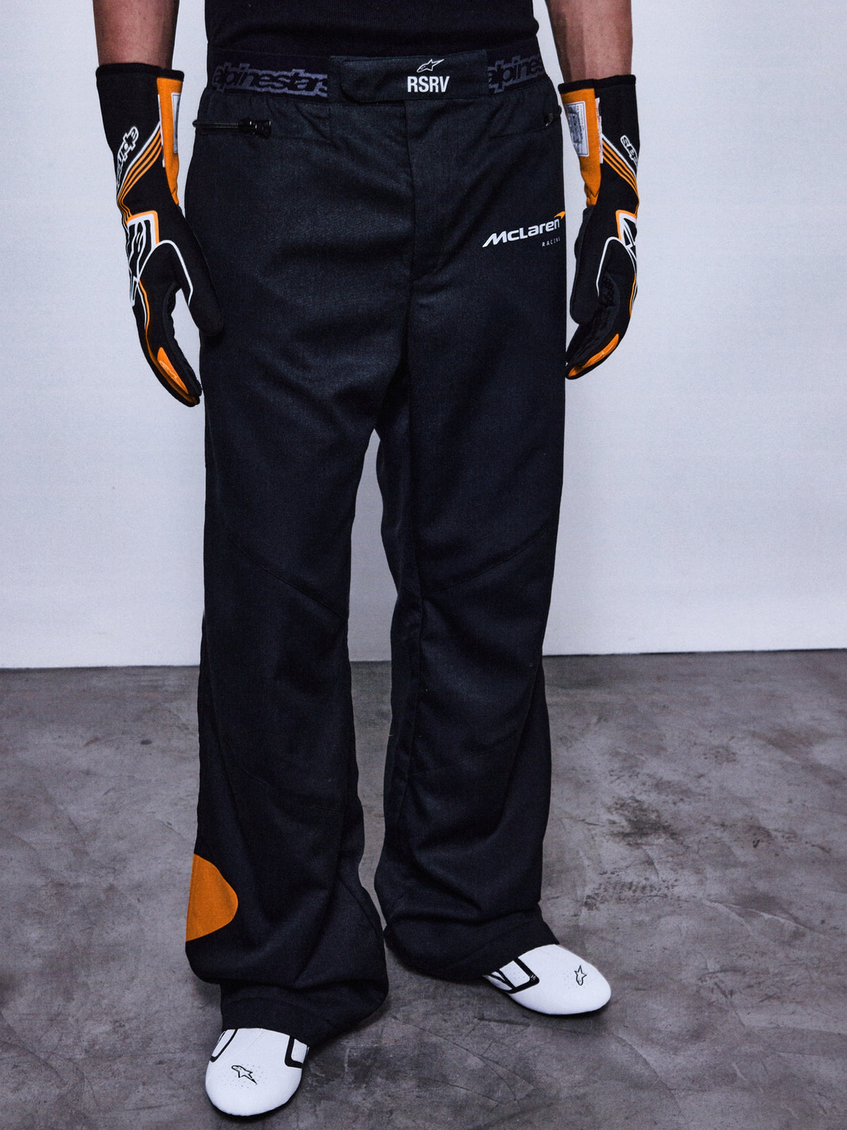 RSRV Arena Suit Pants, Schwarze Rennhose, McLaren und Alpinestars Logos, Orange Patches an der Seite, Orange Kniedetail, Motorsport-Performance-Hose
