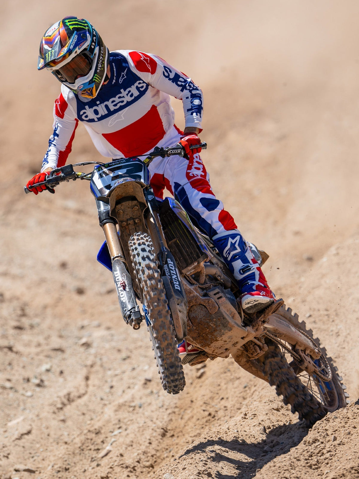 Alpinestars Limited Edition Techstar Fortitude Hose, Motocross-Hose, Hellrot, Weiß und Blau, getragen von einem Fahrer in Aktion auf einer Motocross-Strecke, mit passendem Trikot und Stiefeln, leistungsstarke Offroad-Rennausrüstung.