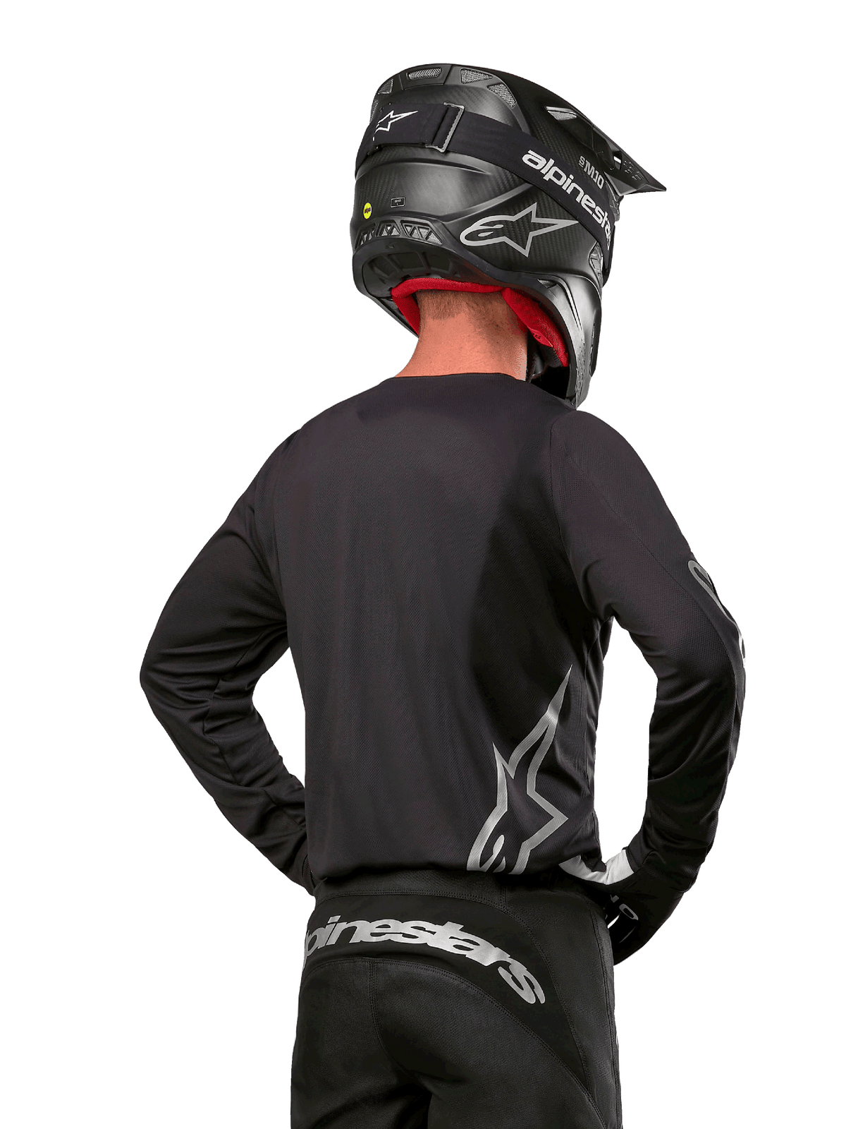 Motocross-Fahrer in der Rückansicht, trägt das Alpinestars 2024 Fluid Graphite Jersey in Black Silver mit einem großen silbernen Logo an der Seite, kombiniert mit einem schwarzen Helm in Carbon-Optik und einer schwarzen Hose, professionelle Offroad-Rennausrüstung