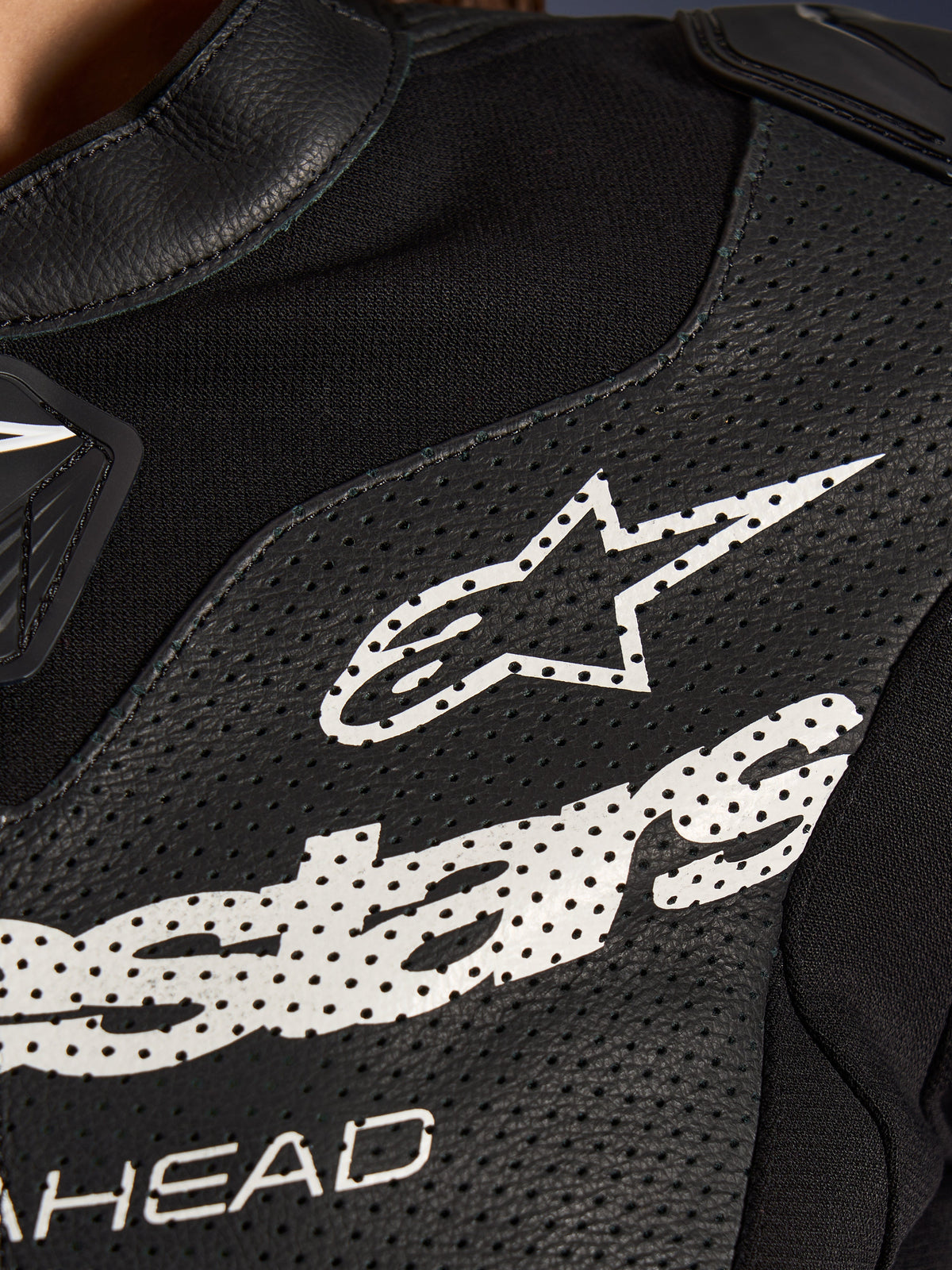 Nahaufnahme des Alpinestars Stella GP-R7 2-Teiler-Lederanzugs in Schwarz, mit perforierten Lederbahnen, einem großen weißen Alpinestars-Logo auf der Brust und atmungsaktiven Stretchgewebe-Abschnitten.