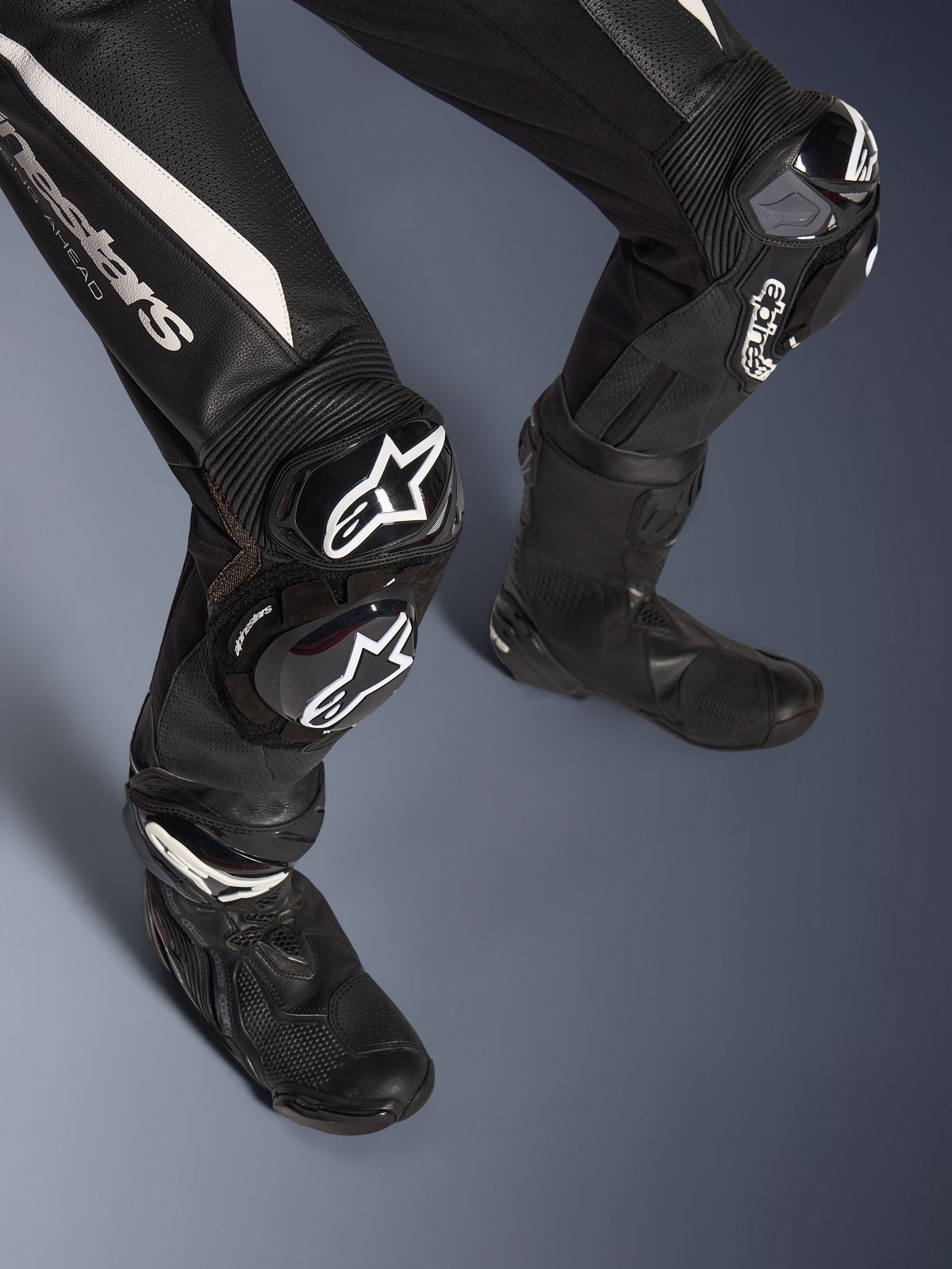 Alpinestars Stella GP-R7 2-Teiler-Lederanzug, Detailansicht der Beine, Schwarz mit weißen Akzenten, GP DFS RR Knieprotektoren und Knieschleifer mit Alpinestars-Logo, kombiniert mit schwarzen Rennstiefeln, entwickelt für Performance auf der Rennstrecke