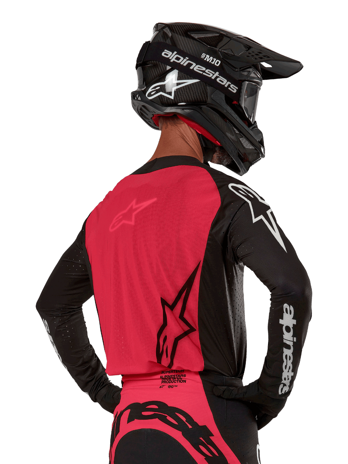Alpinestars 2024 Supertech Ward Trikot, Motocross-Trikot, Schwarz und Red Berry, Rückansicht mit rotem Mesh-Einsatz und schwarzen Ärmeln mit weißem Branding, getragen mit schwarzem Carbon-Helm und Handschuhen, athletische Rennpassform für den Offroad-Einsatz