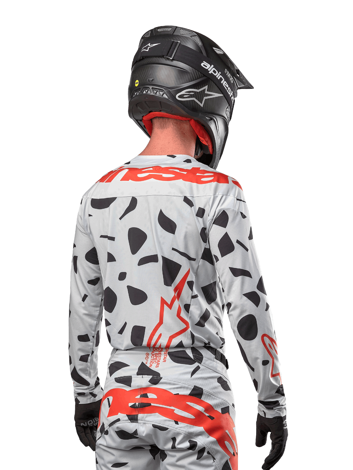 Motocross-Fahrer von hinten im Alpinestars 2024 Techstar Rantera Jersey in Haze Gray Camo, mit einer hellgrauen Basis, schwarzen Grafikflecken und markanten roten Alpinestars-Logos auf dem Rücken und den Schultern, kombiniert mit der passenden Hose und einem schwarzen Helm.