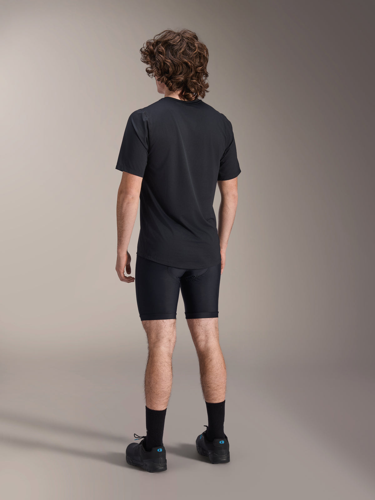 Alpinestars A-Dura Liner Shorts, schwarze Radsport-Innenhose, Rückansicht am Modell, eng anliegendes Stretchgewebe mit sichtbaren Sitzpolsternähten, kombiniert mit einem schwarzen T-Shirt und Radschuhen, Mountainbike-Bekleidung
