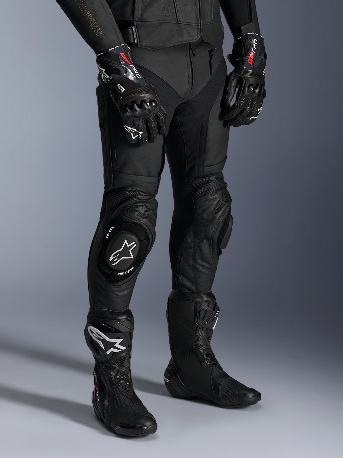 Alpinestars Missile V3 Lederhose, schwarze Motorrad-Rennhose, getragen mit passenden GP Pro Handschuhen und technischen Rennstiefeln, hochwertige Lederkonstruktion mit weißen Logo-Knieschleifern, professionelle Rennsport-Ästhetik für Rennstrecke und Straße
