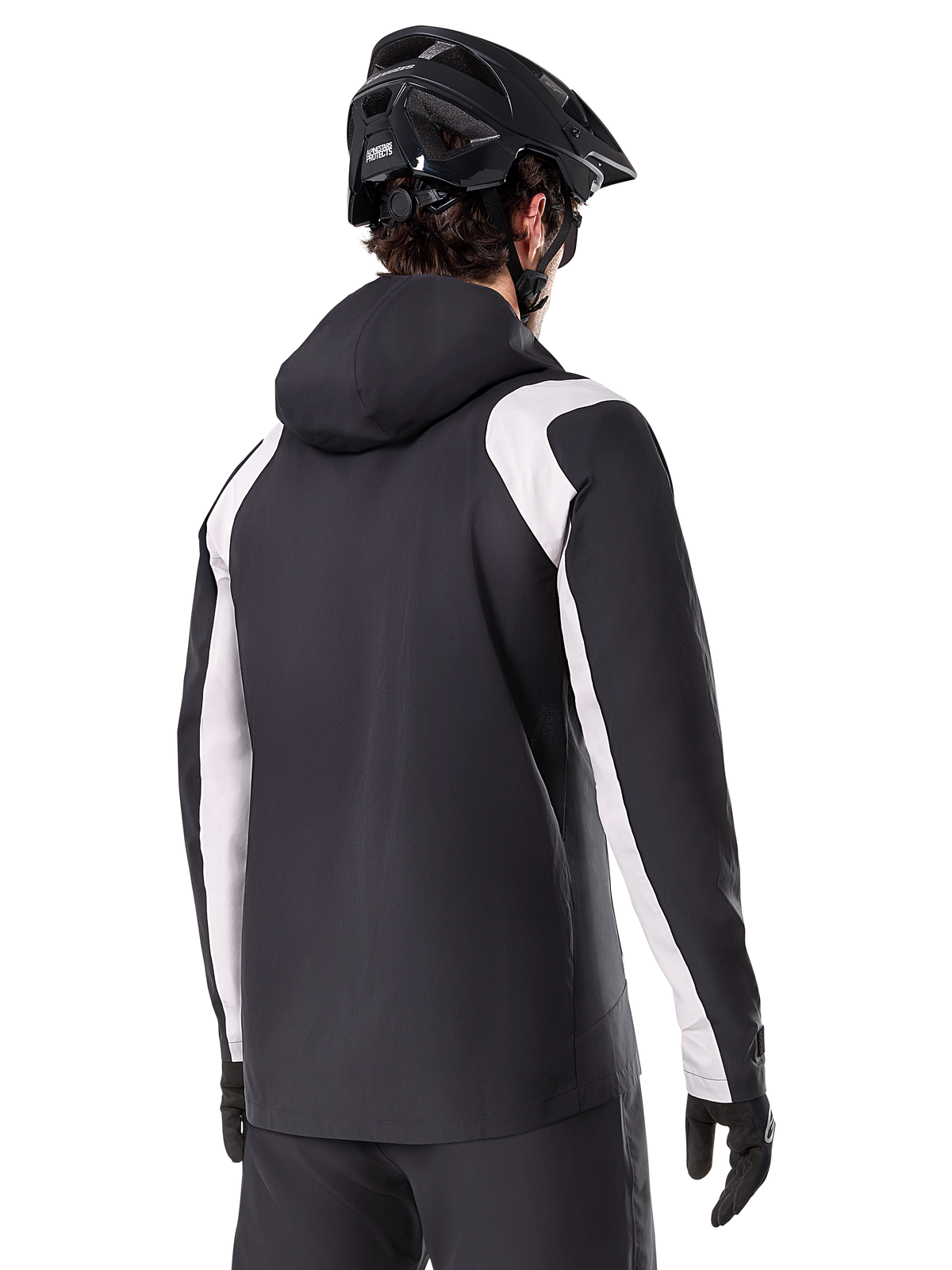 Alpinestars A-Dura Regenjacke, Mountainbike-Regenjacke, Schwarz mit weißen Ärmeleinsätzen, Rückansicht eines Fahrers mit schwarzem MTB-Helm und Handschuhen, technische wasserdichte 2,5-Lagen-Konstruktion, Mountainbike-Bekleidung