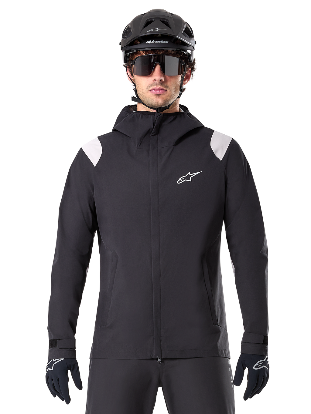 Alpinestars A-Dura Regenjacke, MTB-Regenjacke, Schwarz mit weißen Schultereinsätzen, getragen mit schwarzem MTB-Helm, Sonnenbrille und Handschuhen, wasserdichtes Design mit Kapuze und Frontreißverschluss, sportliche Outdoor-Ausrüstung für den Radsport