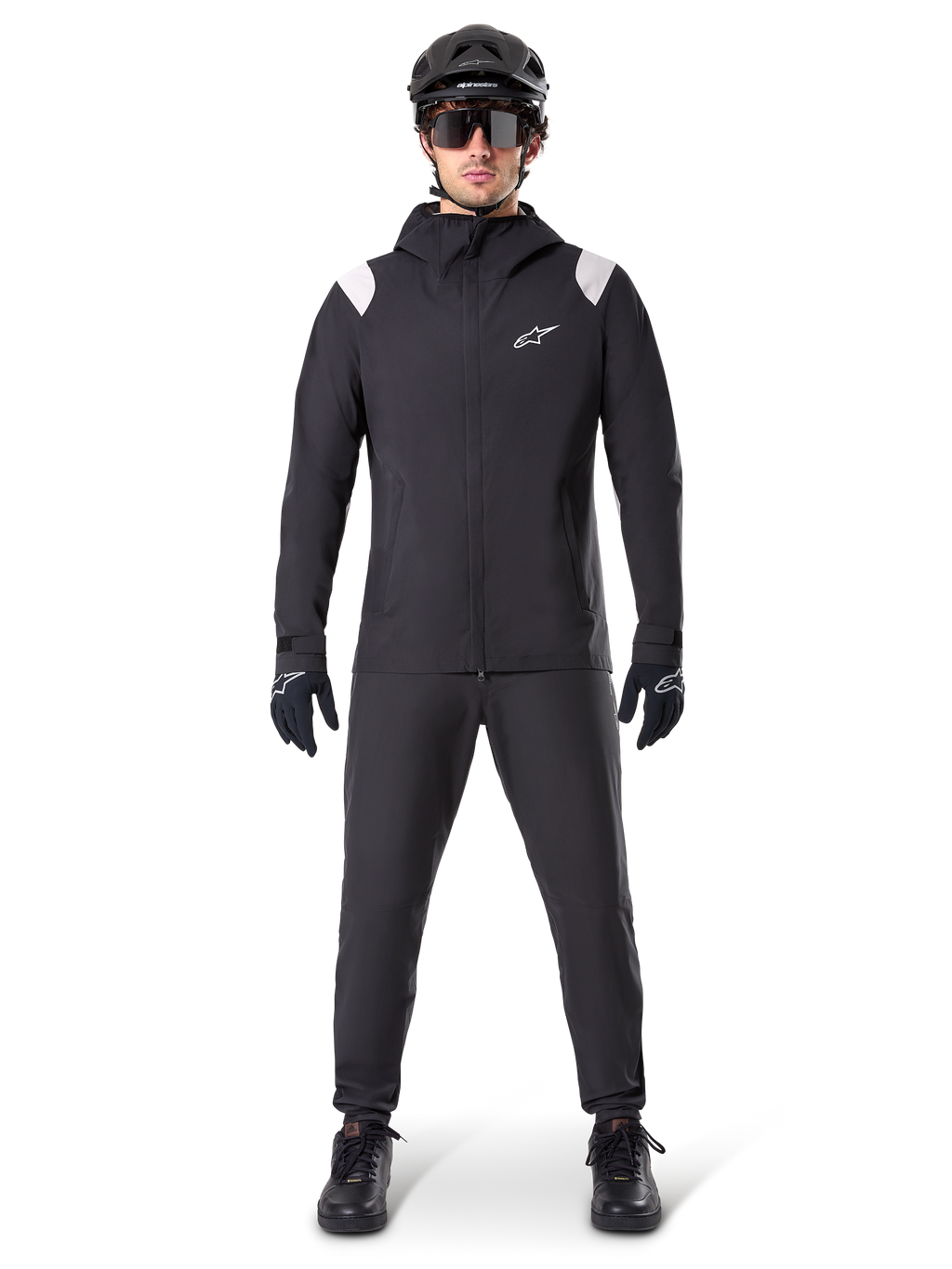 Alpinestars A-Dura Regenjacke, Mountainbike-Regenjacke, Schwarz mit weißen Schulterakzenten und weißem Logo auf der Brust, getragen mit schwarzer Hose, schwarzem Helm, Sonnenbrille und Handschuhen, abgestimmte Mountainbike-Ausrüstung für nasses Wetter