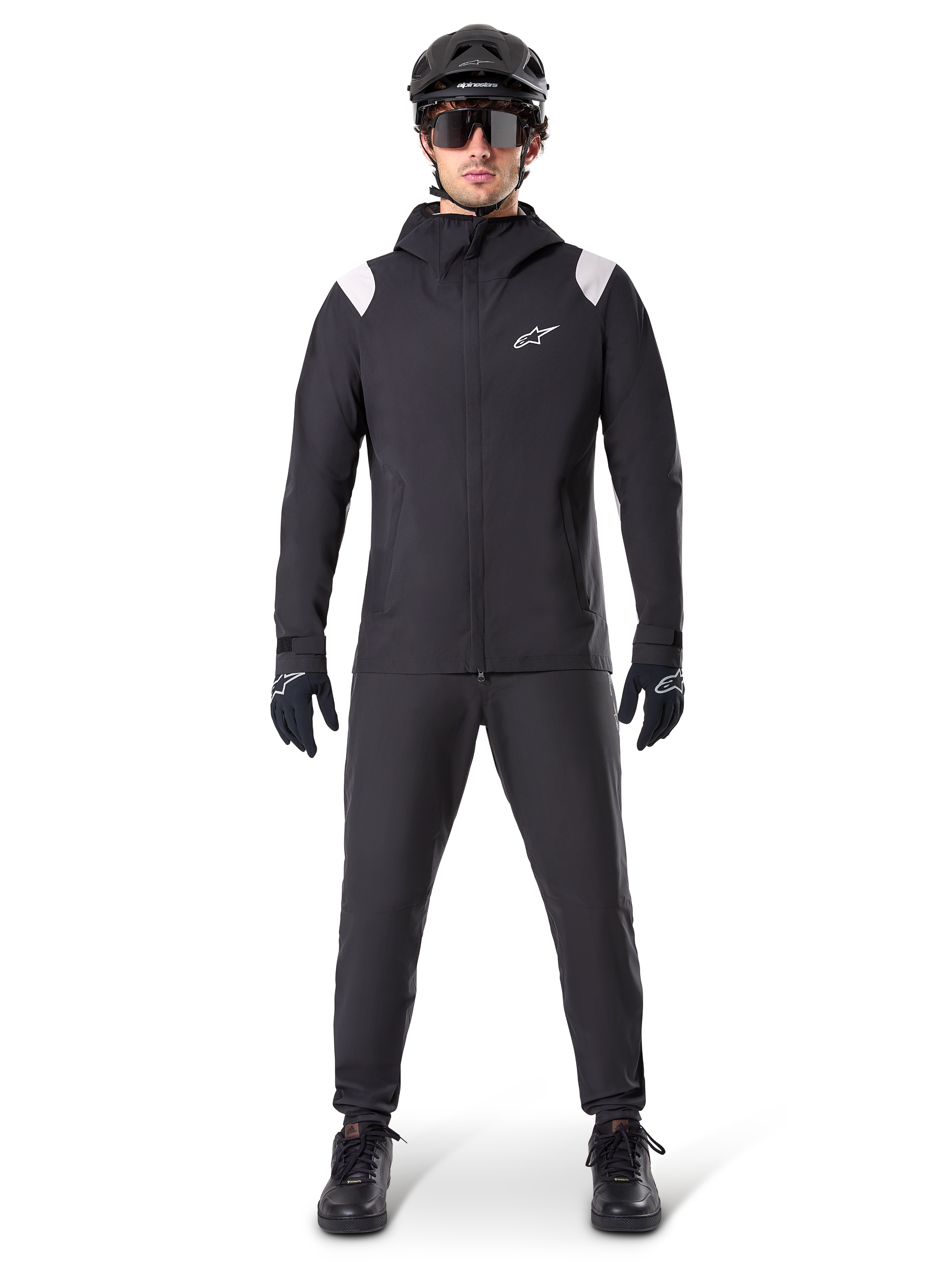 Alpinestars A-Dura Regenjacke, Mountainbike-Regenjacke, Schwarz mit weißen Schulterakzenten und weißem Logo auf der Brust, getragen mit schwarzer Hose, schwarzem Helm, Sonnenbrille und Handschuhen, abgestimmte Mountainbike-Ausrüstung für nasses Wetter