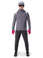 Alpinestars A-Dura Regenjacke, Mountainbike-Jacke, Dunkles Titangrau mit pinkem Logo, getragen mit grauem MTB-Helm und leuchtend pinken Handschuhen, schützendes 2,5-Lagen-Membran-Design für Radsport bei nassem Wetter