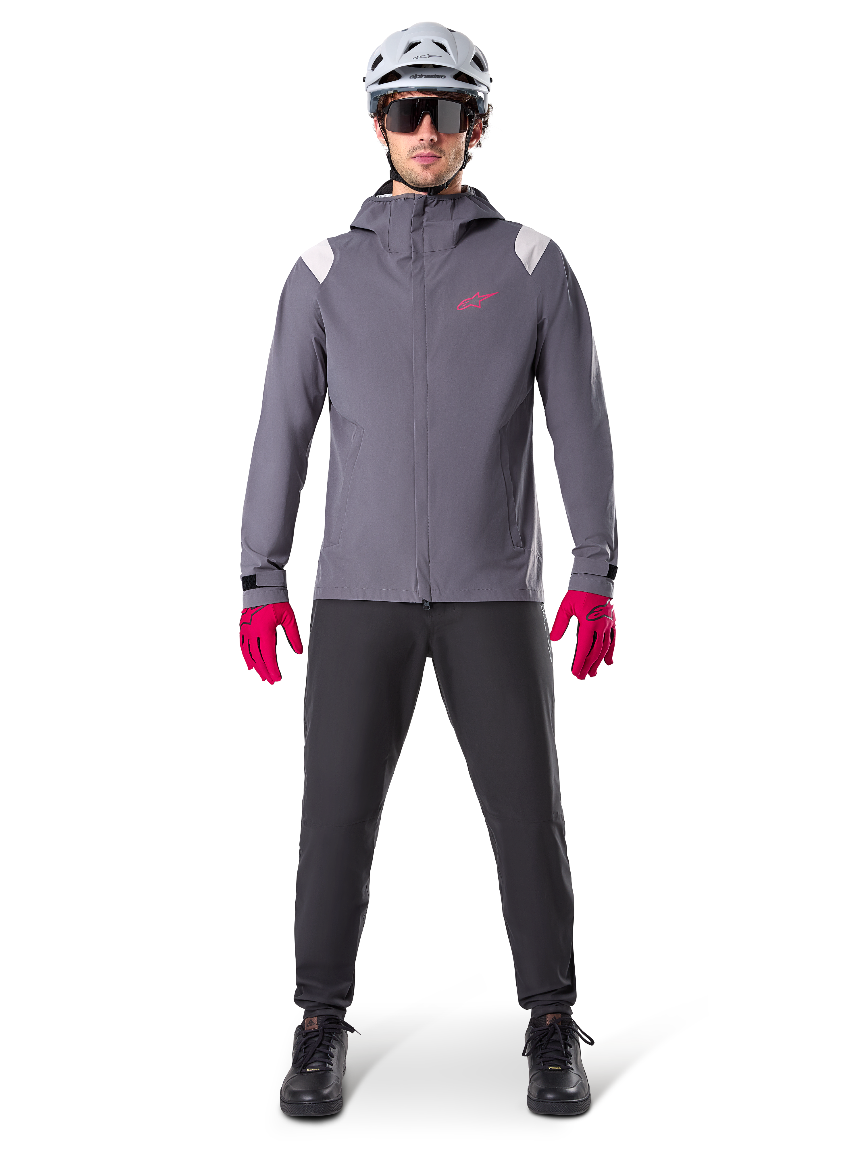 Alpinestars A-Dura Regenjacke, Mountainbike-Jacke, Dunkles Titangrau mit pinkem Logo, getragen mit grauem MTB-Helm und leuchtend pinken Handschuhen, schützendes 2,5-Lagen-Membran-Design für Radsport bei nassem Wetter