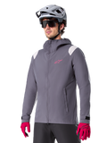 Alpinestars A-Dura Regenjacke, Mountainbike-Regenjacke, Dark Titanium Grau mit pinkem Logo und weißen Schulterakzenten, Kapuzendesign mit Fronttaschen, getragen mit pinken Handschuhen und einem hellgrauen Fahrradhelm