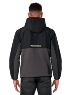 Alpinestars Juncture Hybrid Jacke, Rückansicht, Schwarz und Gunmetal, lässiger Sportswear-Anorak mit Materialmix-Konstruktion, Ripstop-Oberteil und Canvas-Fleece-Unterteil, Alpinestars-Logo auf dem Rücken, getragen mit dunkler Hose