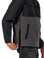 Alpinestars Juncture Hybrid Jacke in Black Gunmetal, seitliche Detailansicht mit Fokus auf den seitlichen Reißverschluss und die untere Leistentasche, Materialmix-Design aus grauem Canvas-Fleece und schwarzen Ripstop-Overlays, lässige vom Motorsport inspirierte Streetwear