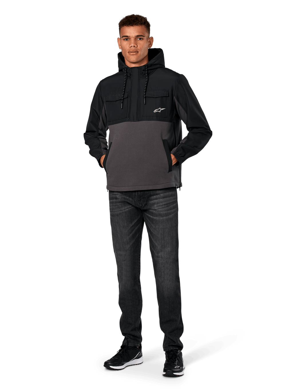 Alpinestars Juncture Hybrid Jacke, Schwarz und Gunmetal, Anorak-Kapuzenpullover aus Mischmaterial mit Canvas-Fleece und Ripstop-Overlays, weißes A-Star Logo auf der Brust, Kapuze mit Kordelzug, Modell trägt dazu dunkle Jeans und schwarze Sneaker, lässige vom Motorsport inspirierte Streetwear