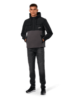 Alpinestars Juncture Hybrid Jacke, Schwarz und Gunmetal, Anorak-Kapuzenpullover aus Mischmaterial mit Canvas-Fleece und Ripstop-Overlays, weißes A-Star Logo auf der Brust, Kapuze mit Kordelzug, Modell trägt dazu dunkle Jeans und schwarze Sneaker, lässige vom Motorsport inspirierte Streetwear