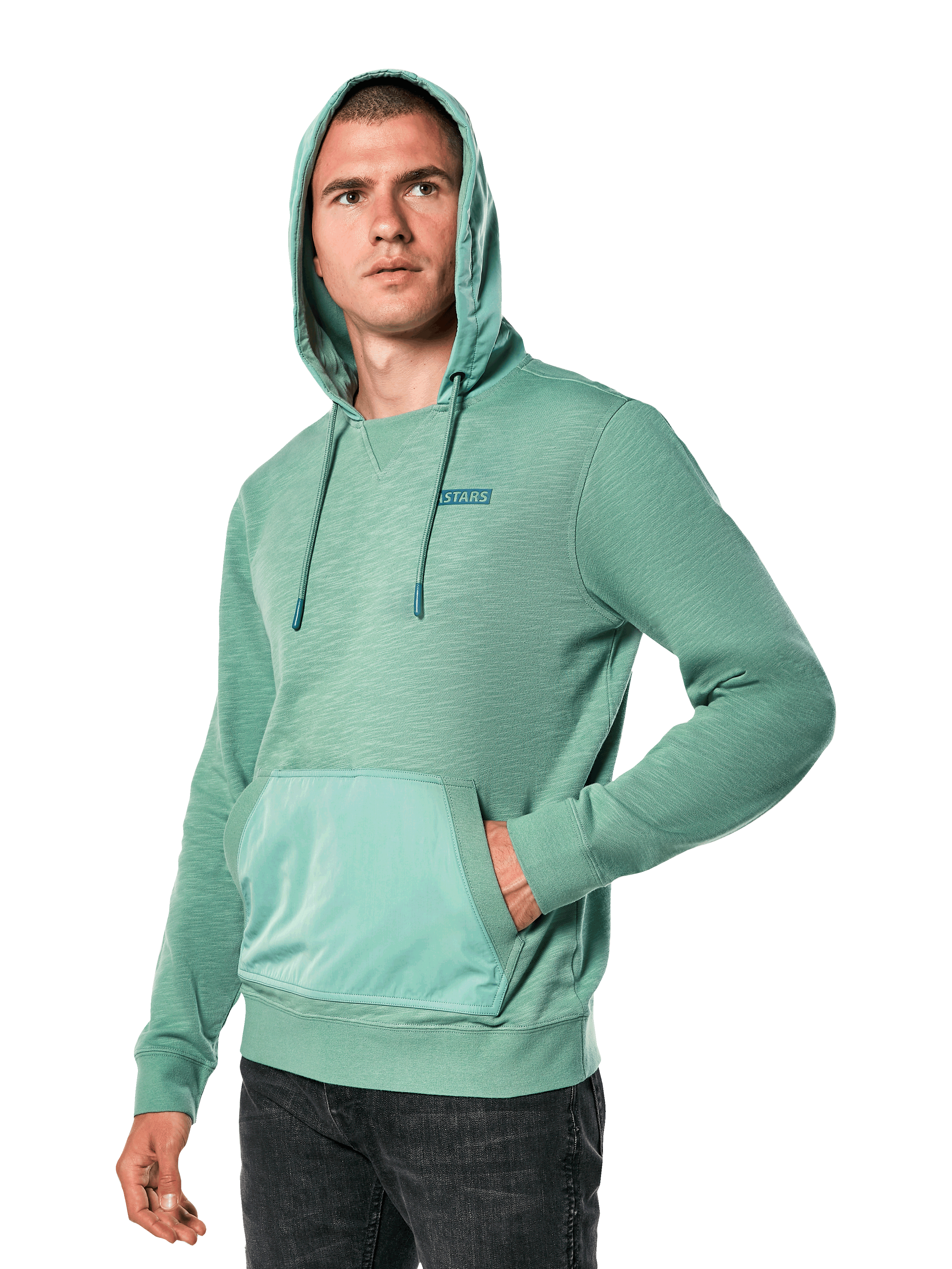 Alpinestars Rooted Hoodie, grünes Slub-French-Terry-Sweatshirt mit Überzugskapuze und Kängurutasche, kleines STARS-Logo auf der Brust, getragen von einem Model mit aufgesetzter Kapuze und Hand in der Tasche, lässige, vom Motorsport inspirierte Streetwear