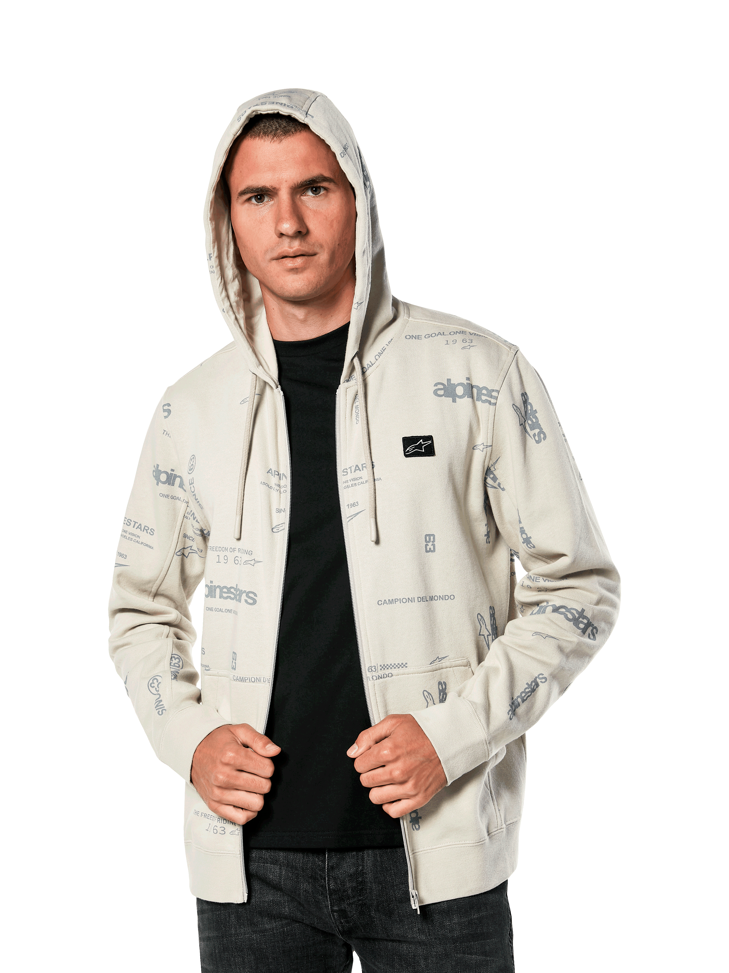 Alpinestars Plenitude Hoodie, lässige Sportbekleidung, Off-White Fleece mit Reißverschluss vorne und grauen Allover-Logo-Grafiken, getragen von einem Mann mit aufgesetzter Kapuze über einem schwarzen Shirt, kleiner Logo-Patch auf der Brust, Kängurutasche