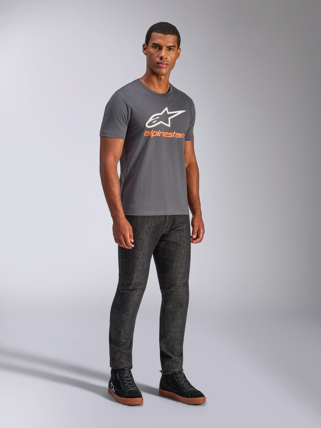 Alpinestars Always 2.0 CSF Tee, Kurzarm-T-Shirt, Anthrazitgrau, weißes A-Star-Logo mit orangefarbenem Branding, lässige Motorsport-Streetwear kombiniert mit dunkler Jeans und schwarzen Sneakern