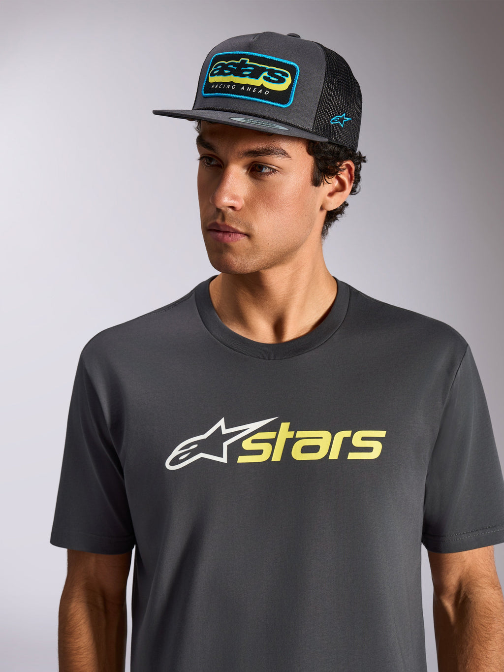Alpinestars Blaze 2.0 CSF Tee, Kurzarm-T-Shirt, Anthrazit mit weißem und Hi-Vis gelbem Logo, getragen mit einer passenden anthrazitfarbenen Mesh-Cap, lässige vom Motorsport inspirierte Sportbekleidung