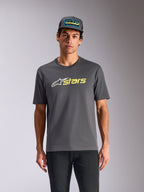 Alpinestars Blaze 2.0 CSF Tee, Kurzarm-T-Shirt, Anthrazitgrau, weißes Stern-Logo und neongelbe „stars“-Grafik, kombiniert mit passender Trucker-Cap und schwarzer Hose, lässige Motorsport-Streetwear