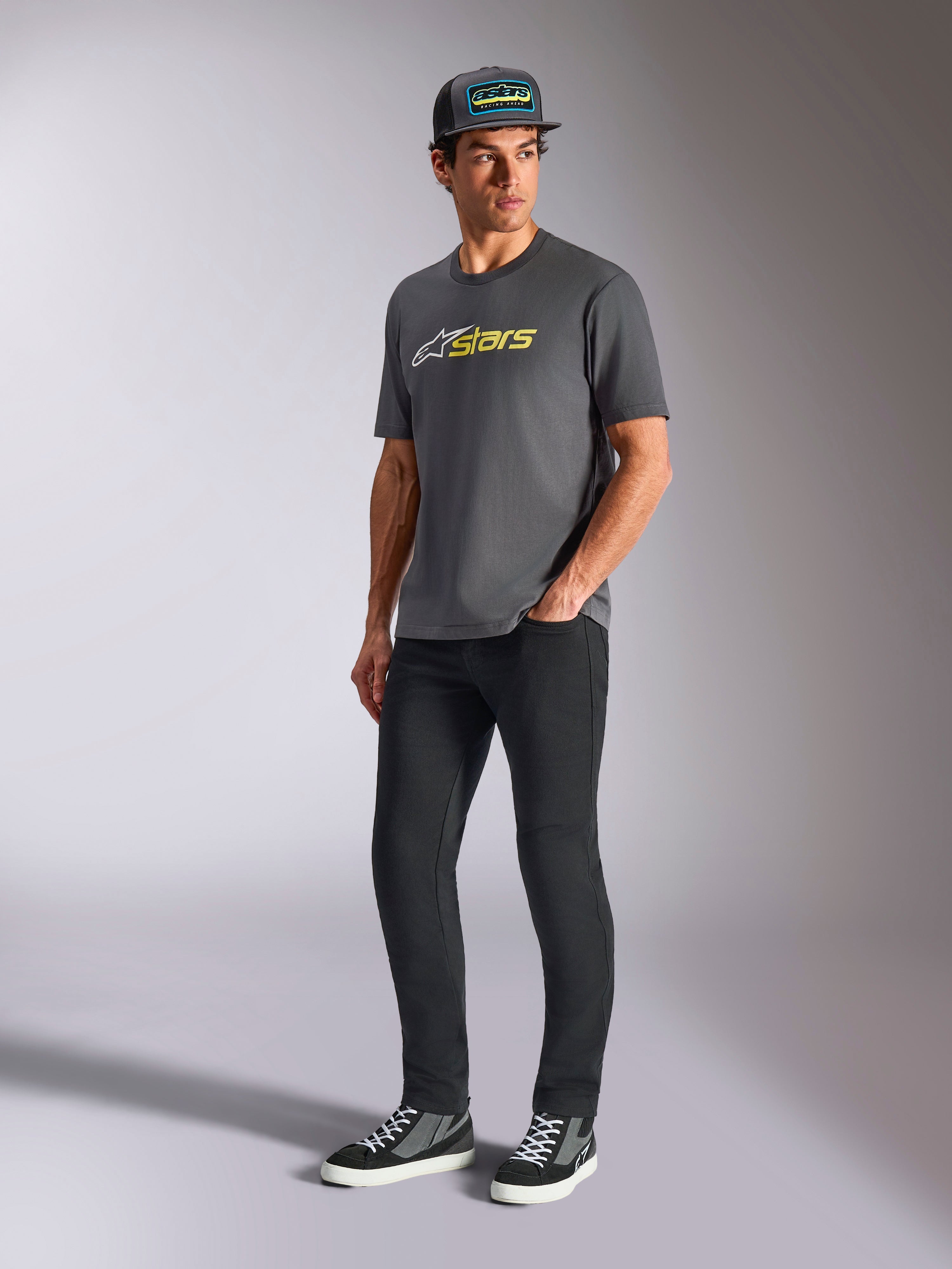 Alpinestars Blaze 2.0 CSF Tee, Kurzarm-T-Shirt, Anthrazitgrau mit weißem und Hi-Vis gelbem Logo, getragen von einem Model mit schwarzer Kappe und Hose, lässige Motorsport-Lifestyle-Bekleidung
