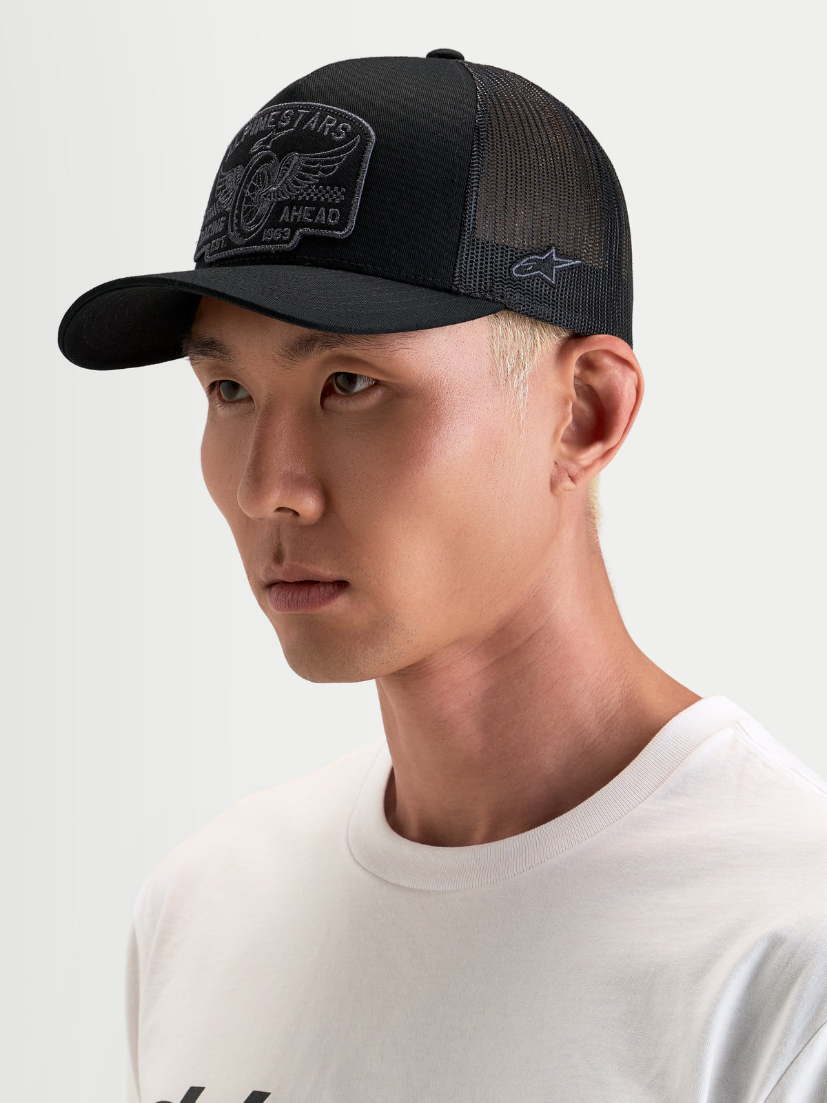 Alpinestars Heritage Patch Trucker-Kappe, schwarze und graue Trucker-Mütze mit gebogenem Schirm, strukturierter Krone und gesticktem Front-Logo-Patch, getragen von einem Model