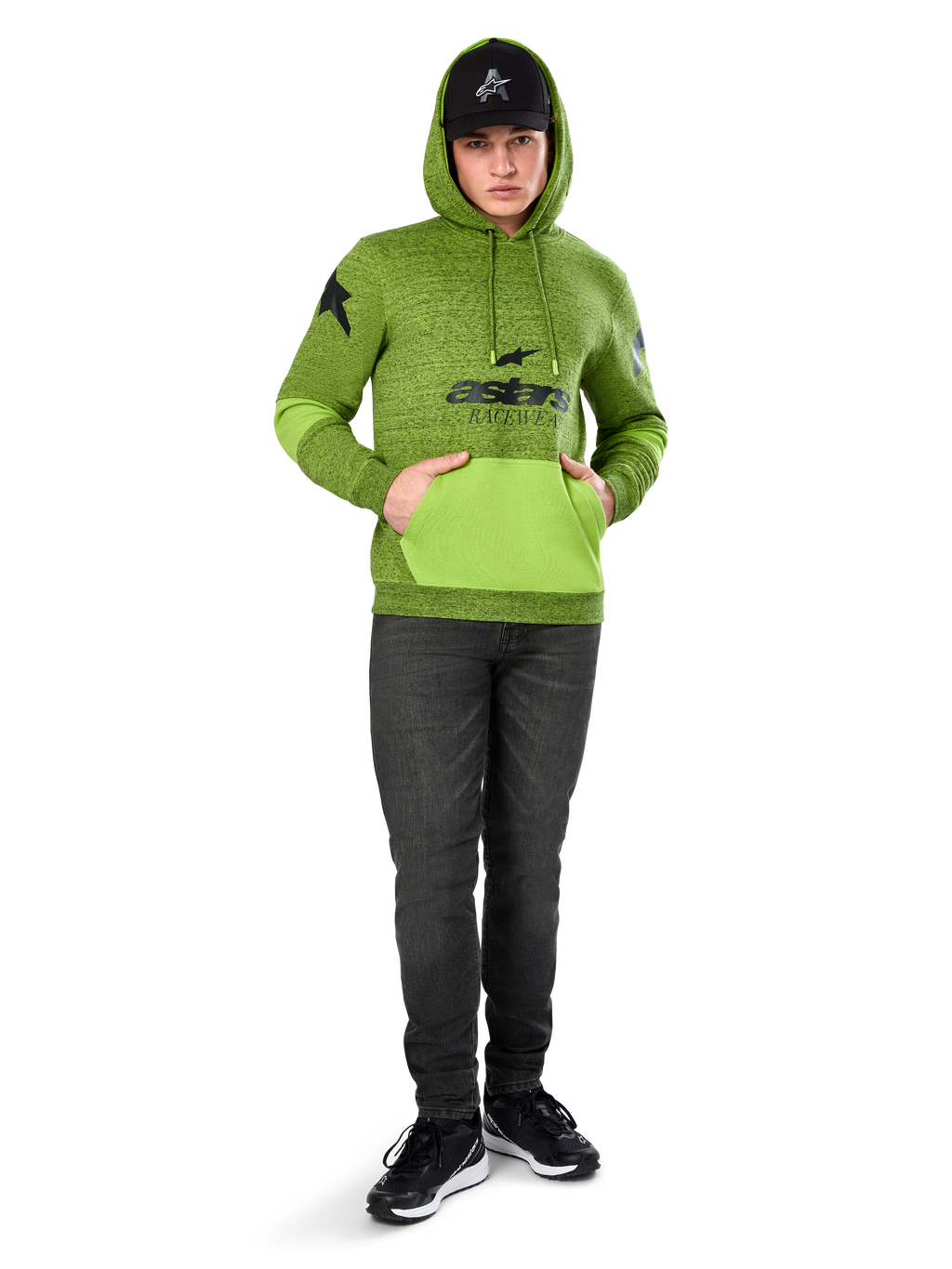 Alpinestars Perpetuate Hoodie, melierter Fleece-Pullover in Lime Green mit kontrastierender hellgrüner Kängurutasche und Ärmeleinsätzen, schwarze „astars“-Grafik auf der Vorderseite, kombiniert mit einer schwarzen Kappe und dunklen Jeans, lässige, vom Motorsport inspirierte Streetwear