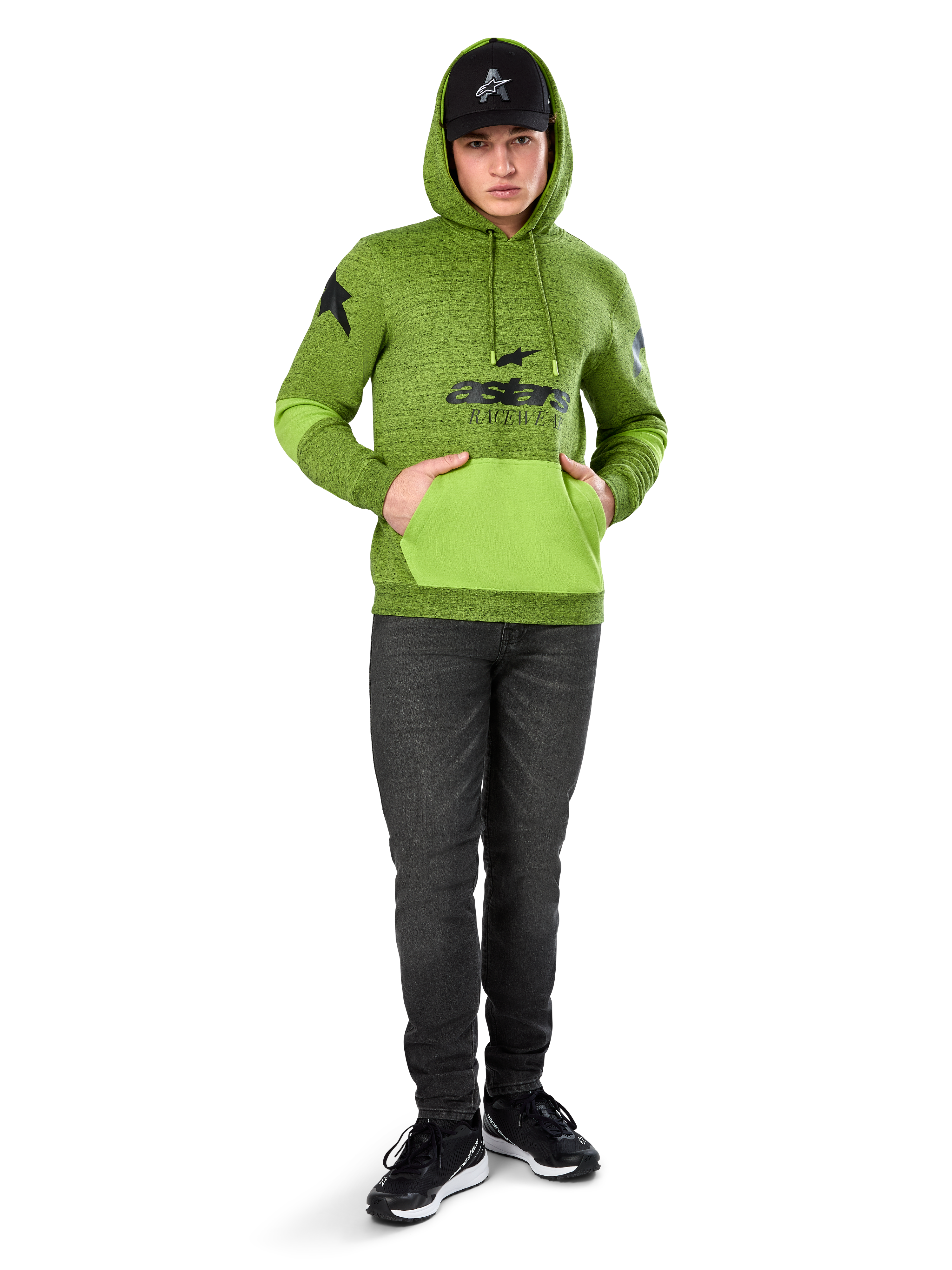 Alpinestars Perpetuate Hoodie, melierter Fleece-Pullover in Lime Green mit kontrastierender hellgrüner Kängurutasche und Ärmeleinsätzen, schwarze „astars“-Grafik auf der Vorderseite, kombiniert mit einer schwarzen Kappe und dunklen Jeans, lässige, vom Motorsport inspirierte Streetwear