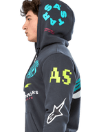 Alpinestars Variegate Hoodie, Fleece-Hoodie mit Reißverschluss in Gunmetal-Grau, Seitenansicht eines Models, Multi-Logo-Artwork in Neongelb, Hellblau und Weiß, mit 'AS'-Branding am Ärmel und 'STARS' auf der Kapuze, lässige Motorsport-inspirierte Streetwear