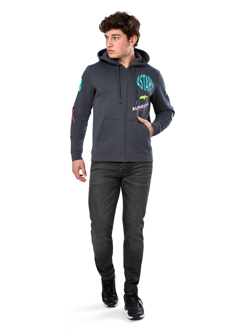 Alpinestars Variegate Hoodie, Fleece-Hoodie mit Reißverschluss, Gunmetal-Grau, getragen von einem Modell mit schwarzen Jeans und Sneakern, mit türkisfarbenem 'ASTARS'-Branding und bunten Logo-Grafiken auf Ärmeln und Brust, lässige Motorsport-Streetwear