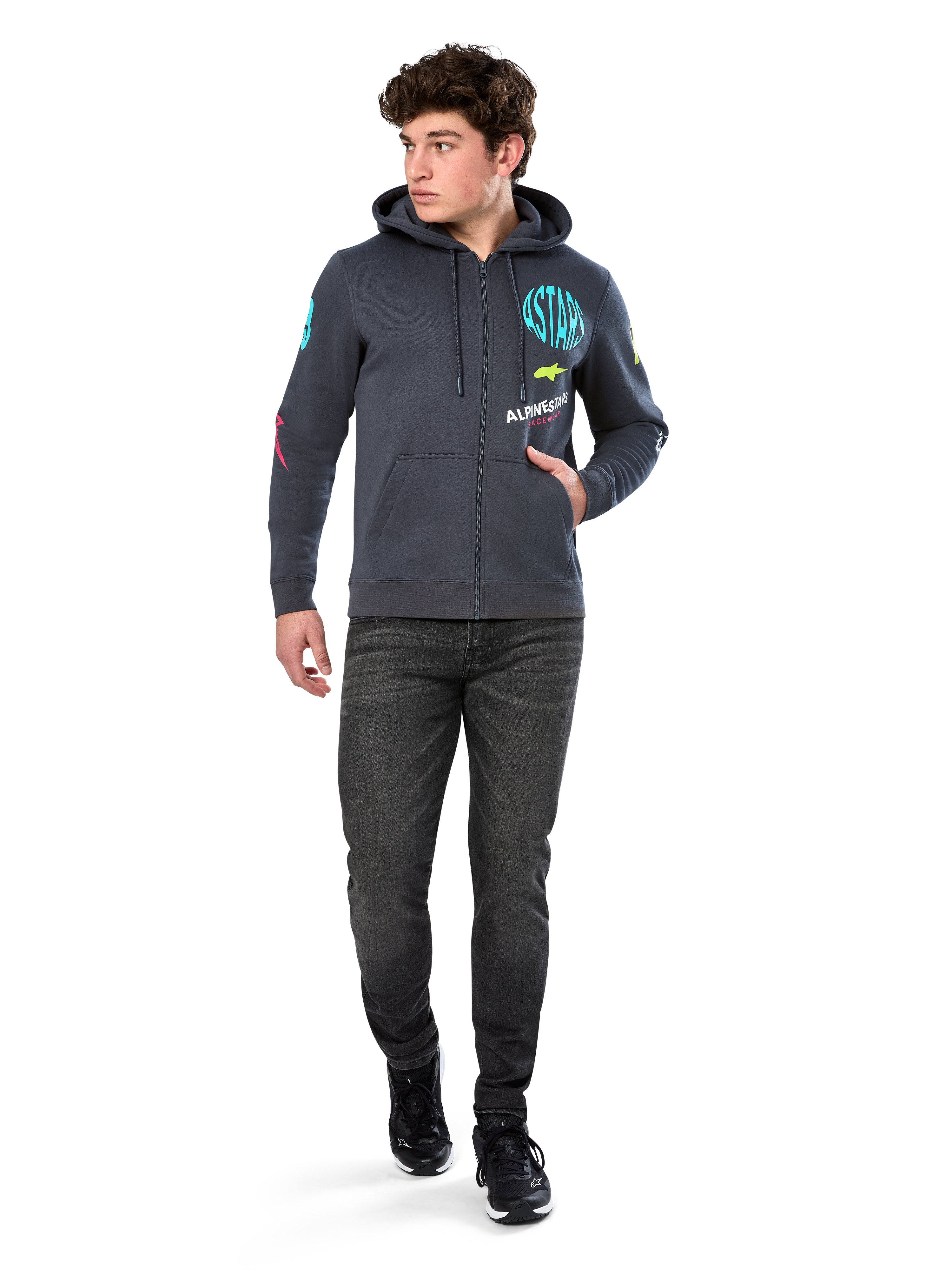 Alpinestars Variegate Hoodie, Fleece-Hoodie mit Reißverschluss, Gunmetal-Grau, getragen von einem Modell mit schwarzen Jeans und Sneakern, mit türkisfarbenem 'ASTARS'-Branding und bunten Logo-Grafiken auf Ärmeln und Brust, lässige Motorsport-Streetwear