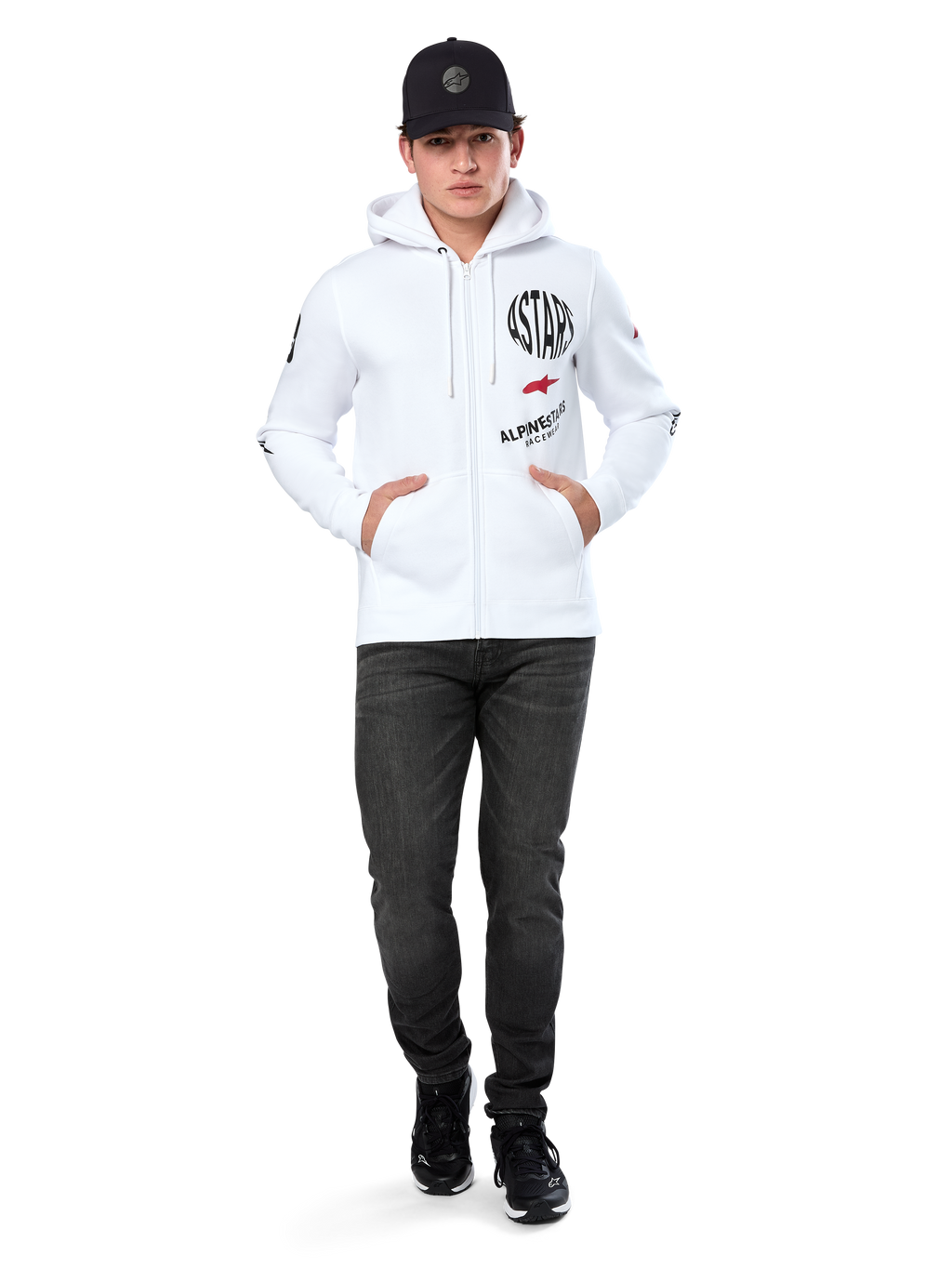 Alpinestars Variegate Hoodie, weißer Fleece-Hoodie mit Reißverschluss, Multi-Logo-Grafik mit „ASTARS“ und rotem Stern-Logo auf der Brust, grafische Details an den Ärmeln, getragen von einem Model mit schwarzer Kappe und schwarzer Jeans, lässige Motorsport-Streetwear