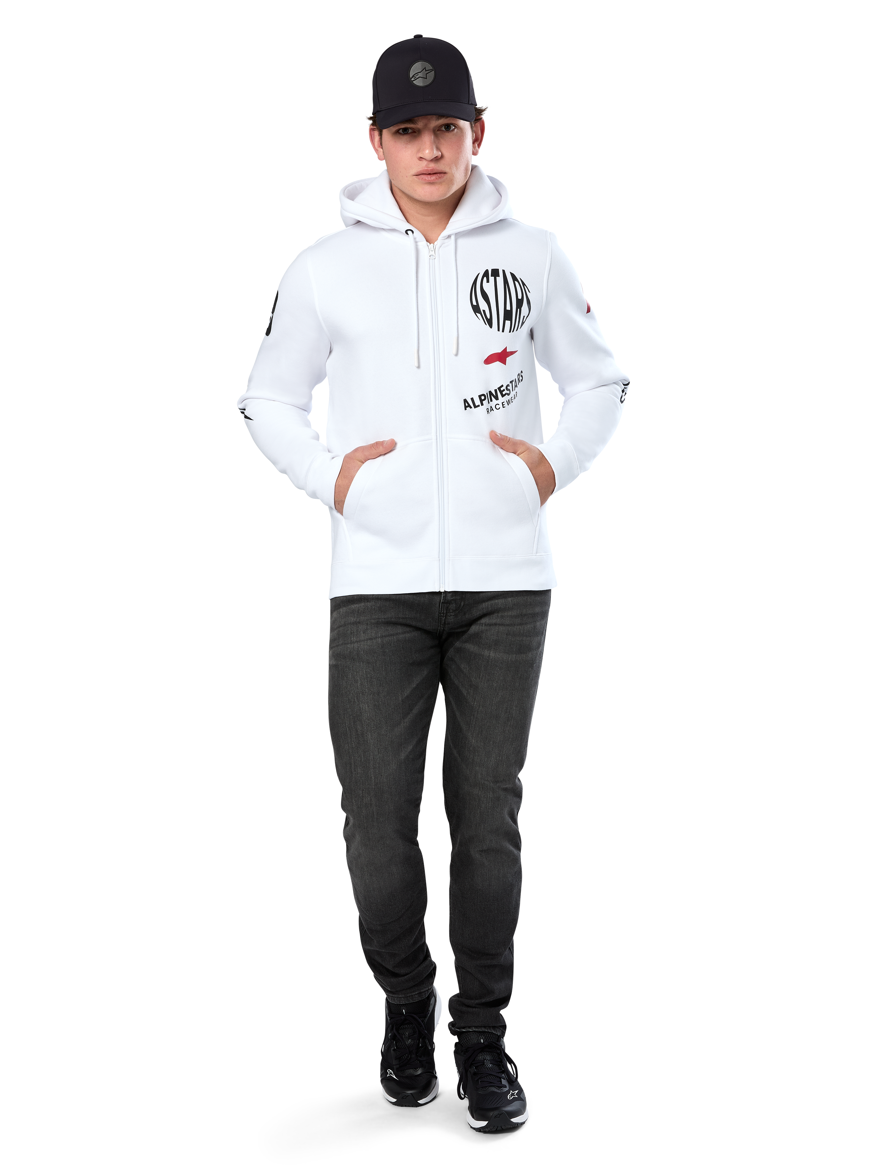 Alpinestars Variegate Hoodie, weißer Fleece-Hoodie mit Reißverschluss, Multi-Logo-Grafik mit „ASTARS“ und rotem Stern-Logo auf der Brust, grafische Details an den Ärmeln, getragen von einem Model mit schwarzer Kappe und schwarzer Jeans, lässige Motorsport-Streetwear