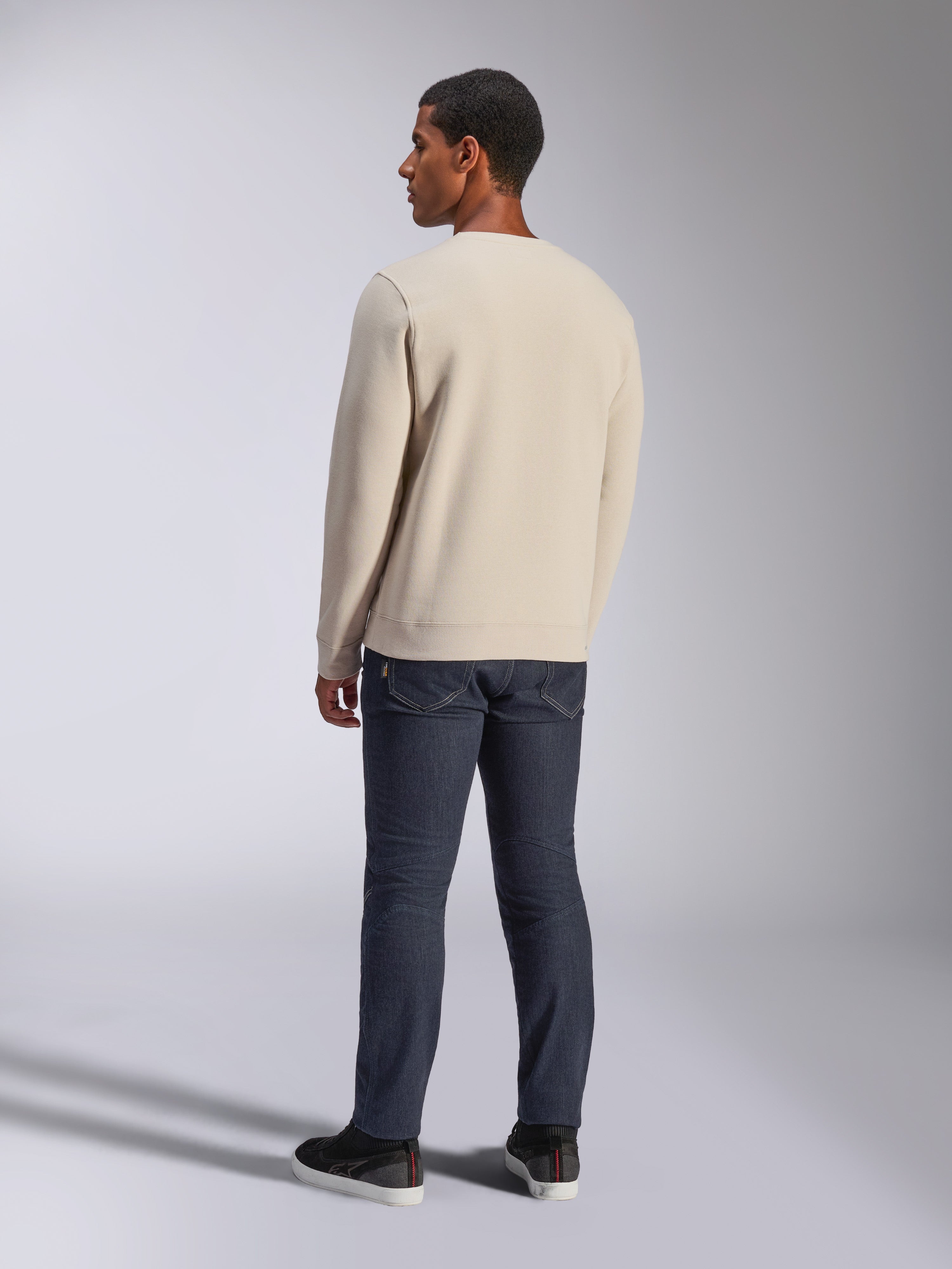 Alpinestars Positive Crew, Off White crewneck sweatshirt, back view on model, paired with dark denim jeans and black sneakers, casual motorsport streetwear, featuring ribbed cuffs and hem
