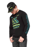 Alpinestars Ayess CSF Langarmshirt, schwarzes Langarmshirt mit neongelben und cyanfarbenen Grafiken, großes AS-Logo auf der Brust und vertikales Alpinestars-Branding am Ärmel, getragen von einem Model mit passender schwarzer Kappe und dunkler Jeans, lässige Motorsport-Lifestyle-Bekleidung