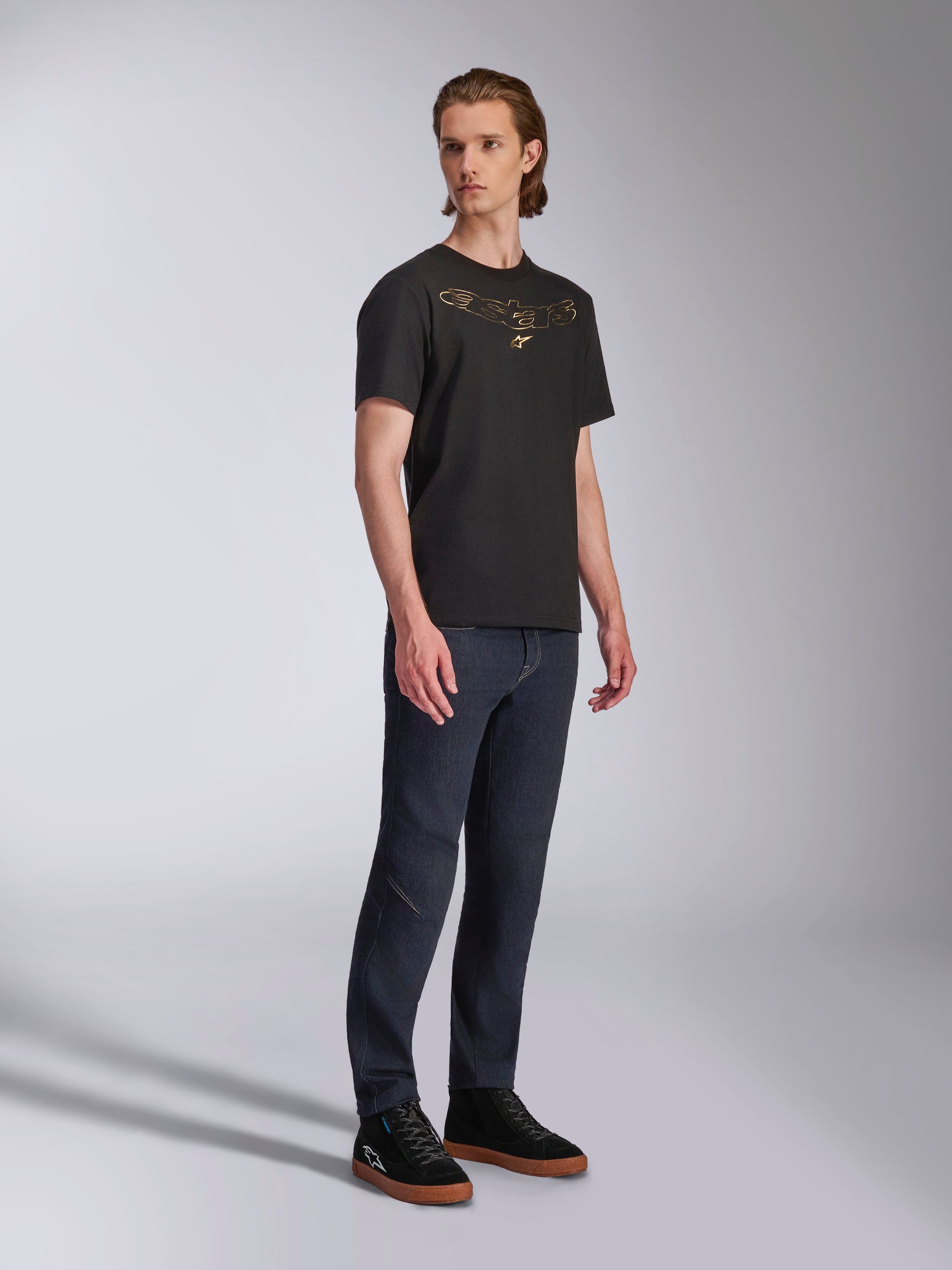 Alpinestars Luxo CSF Tee, Short Sleeve T-Shirt, Black, Gold Astars Outlined Chest Logo, worn by model with dark denim jeans and black sneakers, Casual Motorsport Streetwear