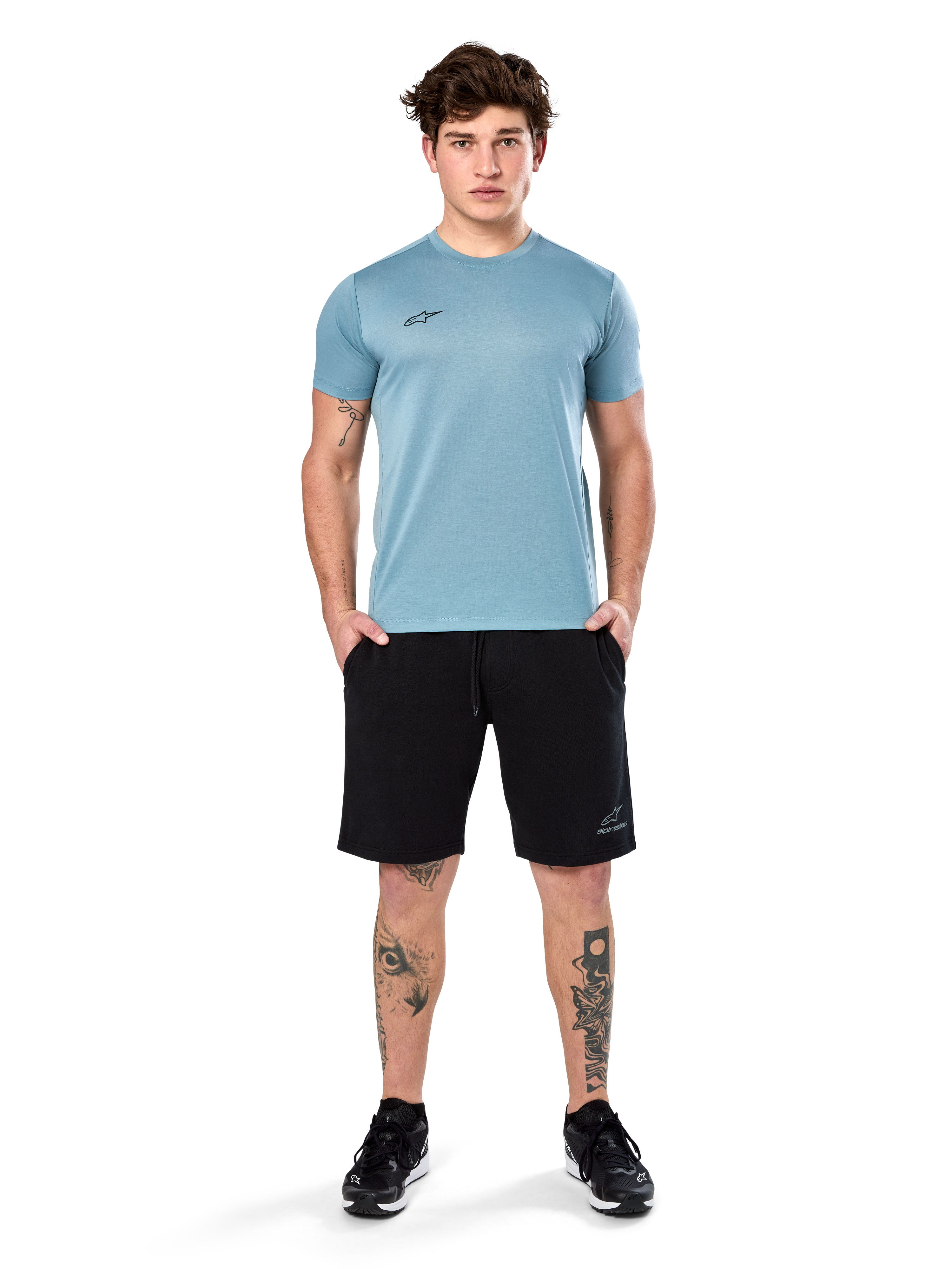 Alpinestars Point Performance Tee, Kurzarm-T-Shirt, Ice Blue, mit kleinem schwarzen Logo vorne, Rundhalsausschnitt, getragen von einem Model mit schwarzen Shorts und schwarzen Sneakern, lässige feuchtigkeitsableitende Sportbekleidung