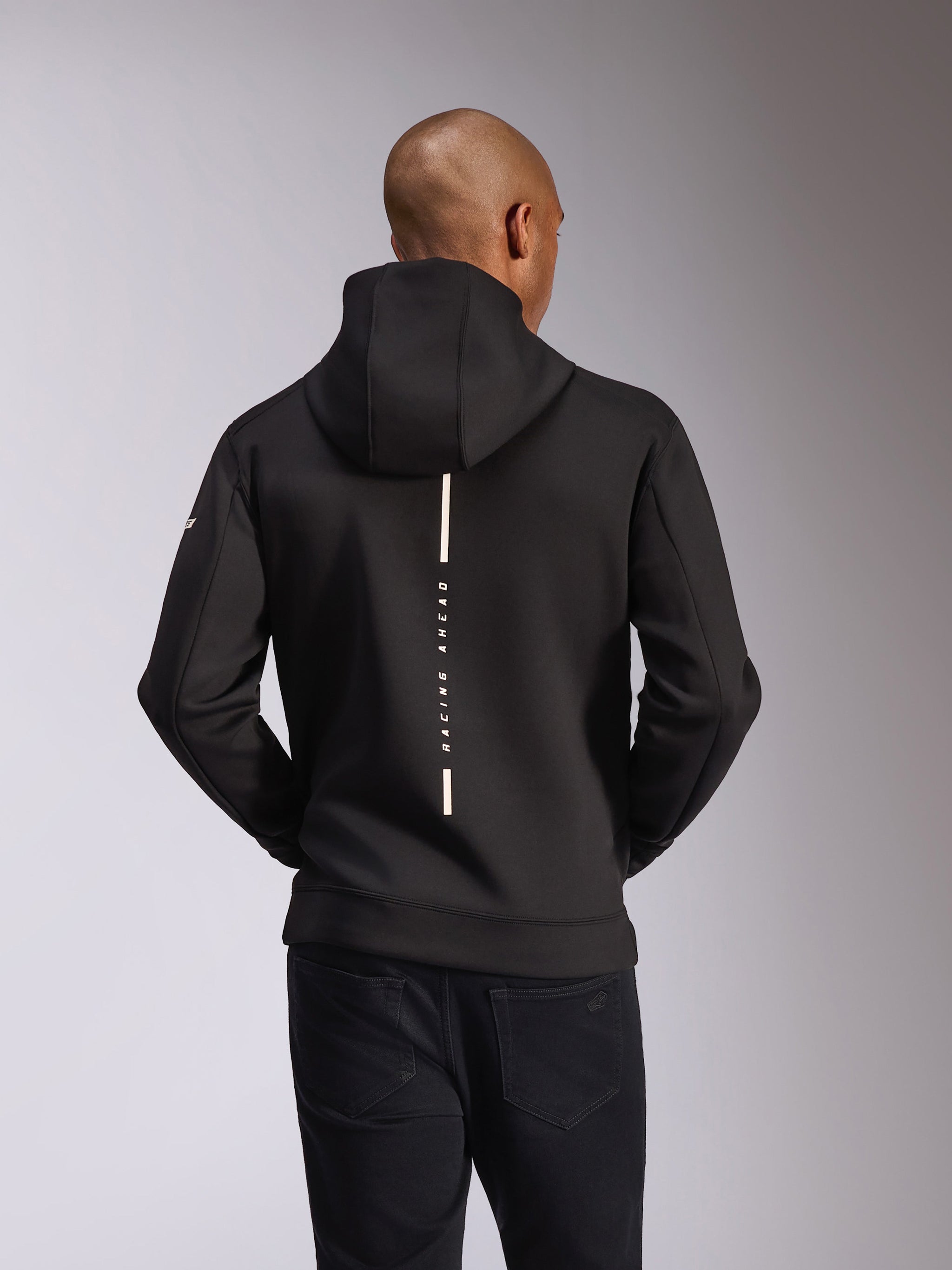 Alpinestars Insight Hoodie, Rückansicht, Schwarz, vertikaler weißer Streifen mit 'RACING AHEAD' Schriftzug, Logo-Branding am Ärmel, lässige, vom Motorsport inspirierte Streetwear