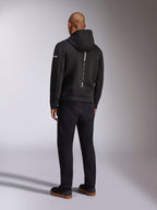 Alpinestars Insight Hoodie, Black sportswear hoodie, back view showing a vertical white stripe with 'RACING AHEAD' branding, sleeve logo, paired with black pants and sneakers, casual motorsport-inspired design