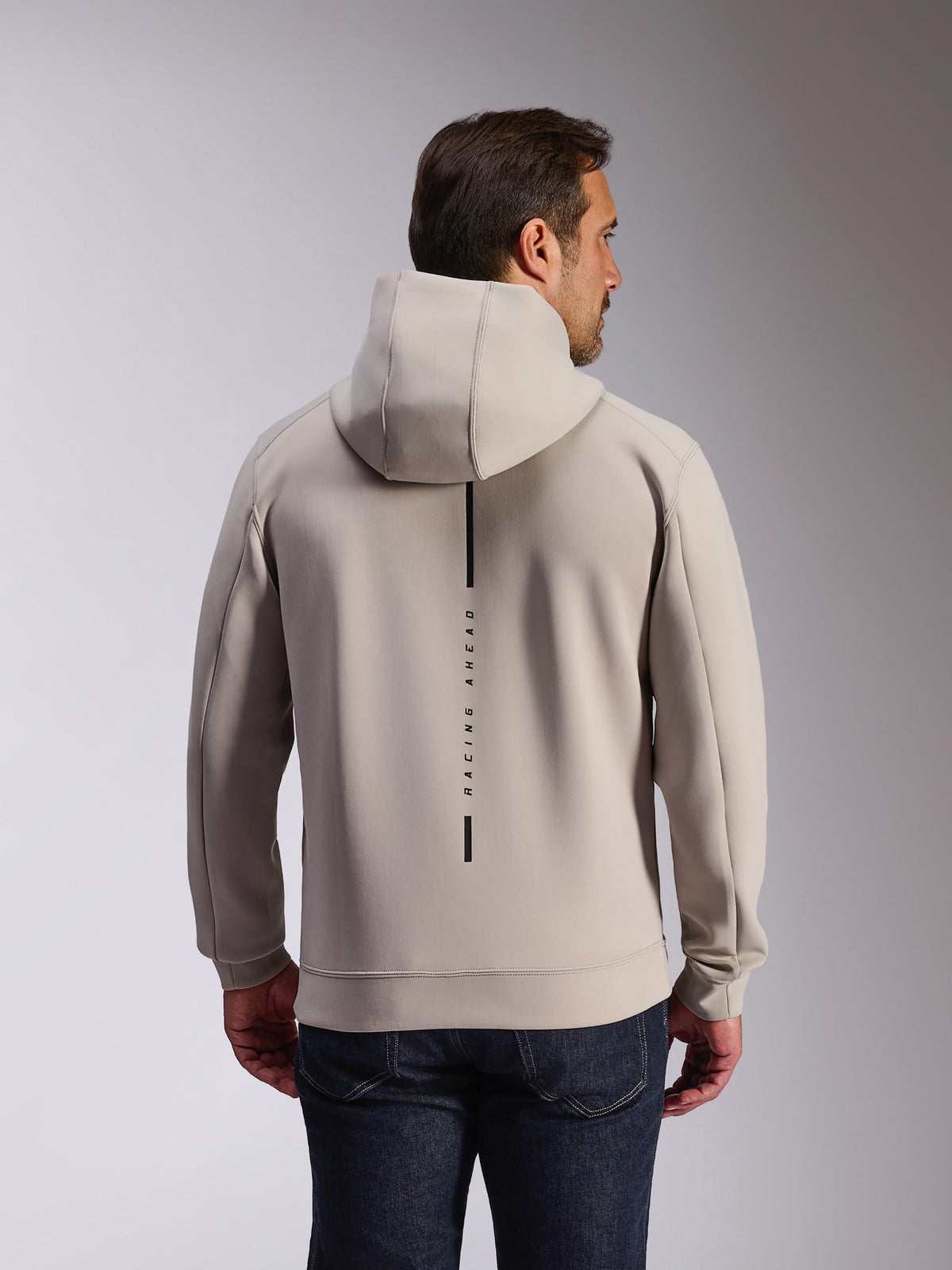 Alpinestars Insight Hoodie in Cement, Rückansicht eines Models in einem hellgrauen Kapuzensweatshirt, schwarzes vertikales Streifen-Logo mit 'RACING AHEAD' Text, lässiger vom Motorsport inspirierter Doppel-Fleece-Hoodie.