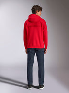 Alpinestars Emergent Oversized Hoodie, Rot, Rückansicht an einem männlichen Model, mit Ton-in-Ton 3D-besticktem Alpinestars-Wortlogo, kombiniert mit dunkelblauen Jeans, lässige motorsport-inspirierte Streetwear